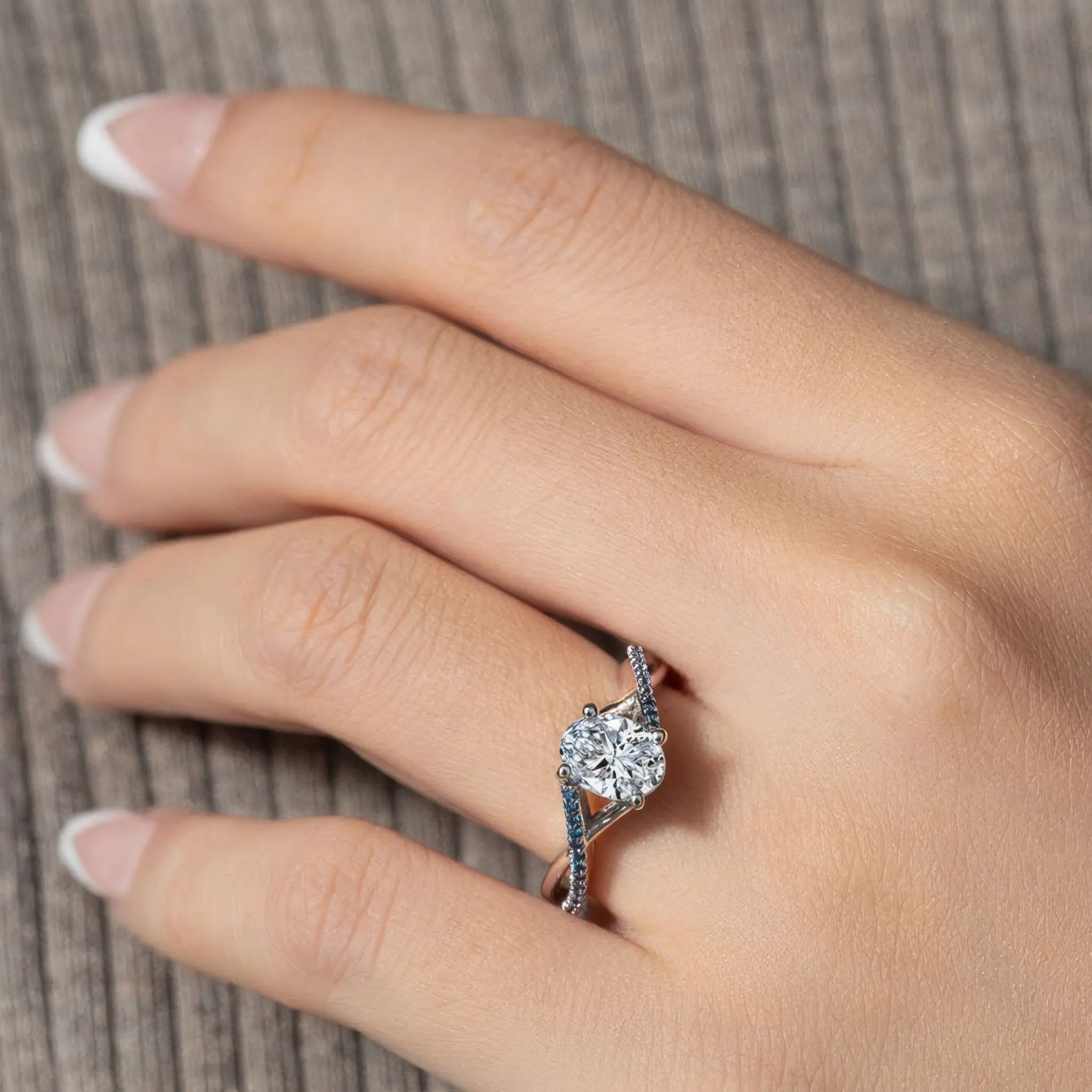 Close-up of a hand wearing a beautiful blue and white diamond engagement ring, showcasing elegant design and sparkle.