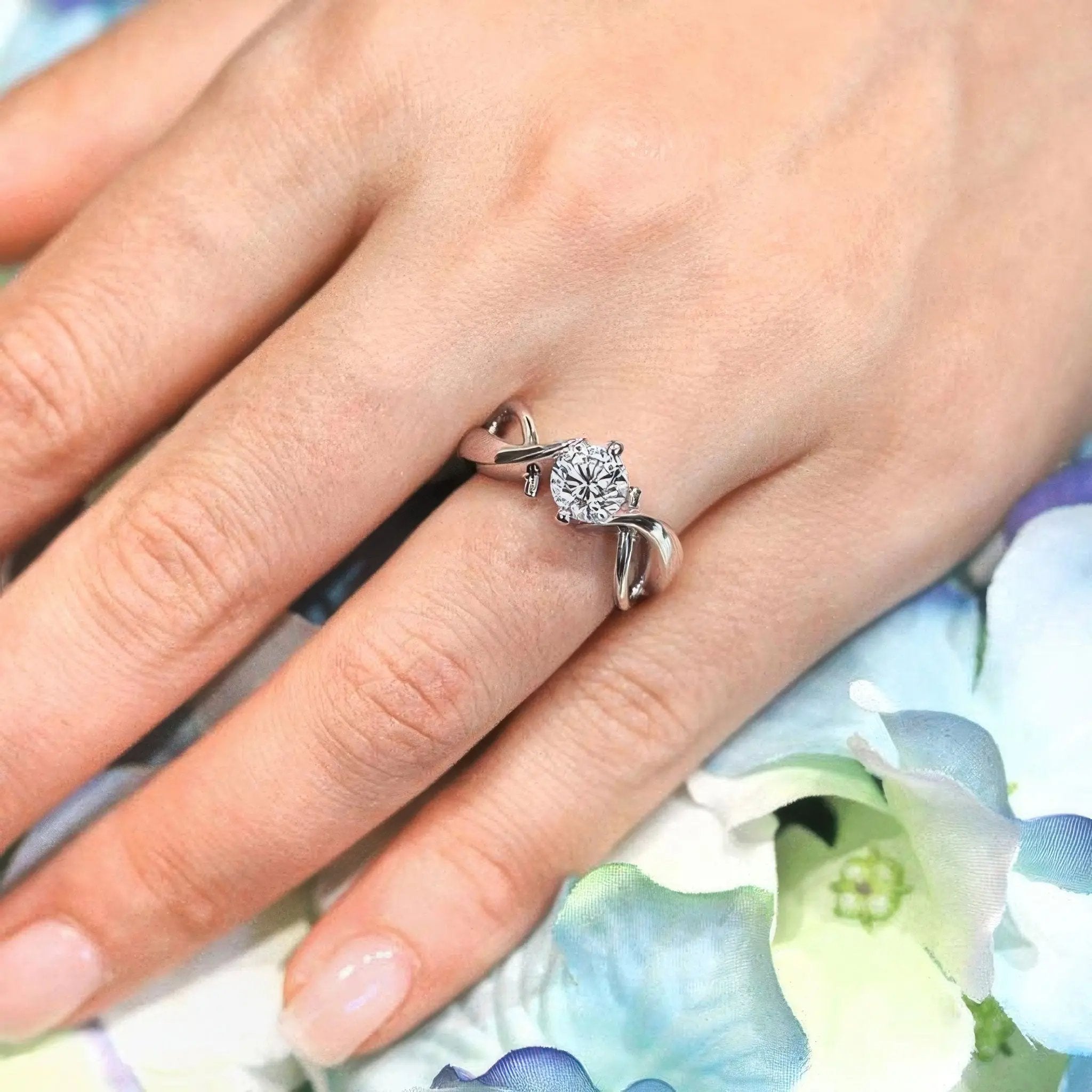 Double wire trim lab diamond solitaire ring with a round center on a delicate hand, surrounded by soft floral decor.