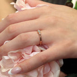Close-up of a hand wearing a white gold three stone promise ring with diamonds, resting on pink rose petals.