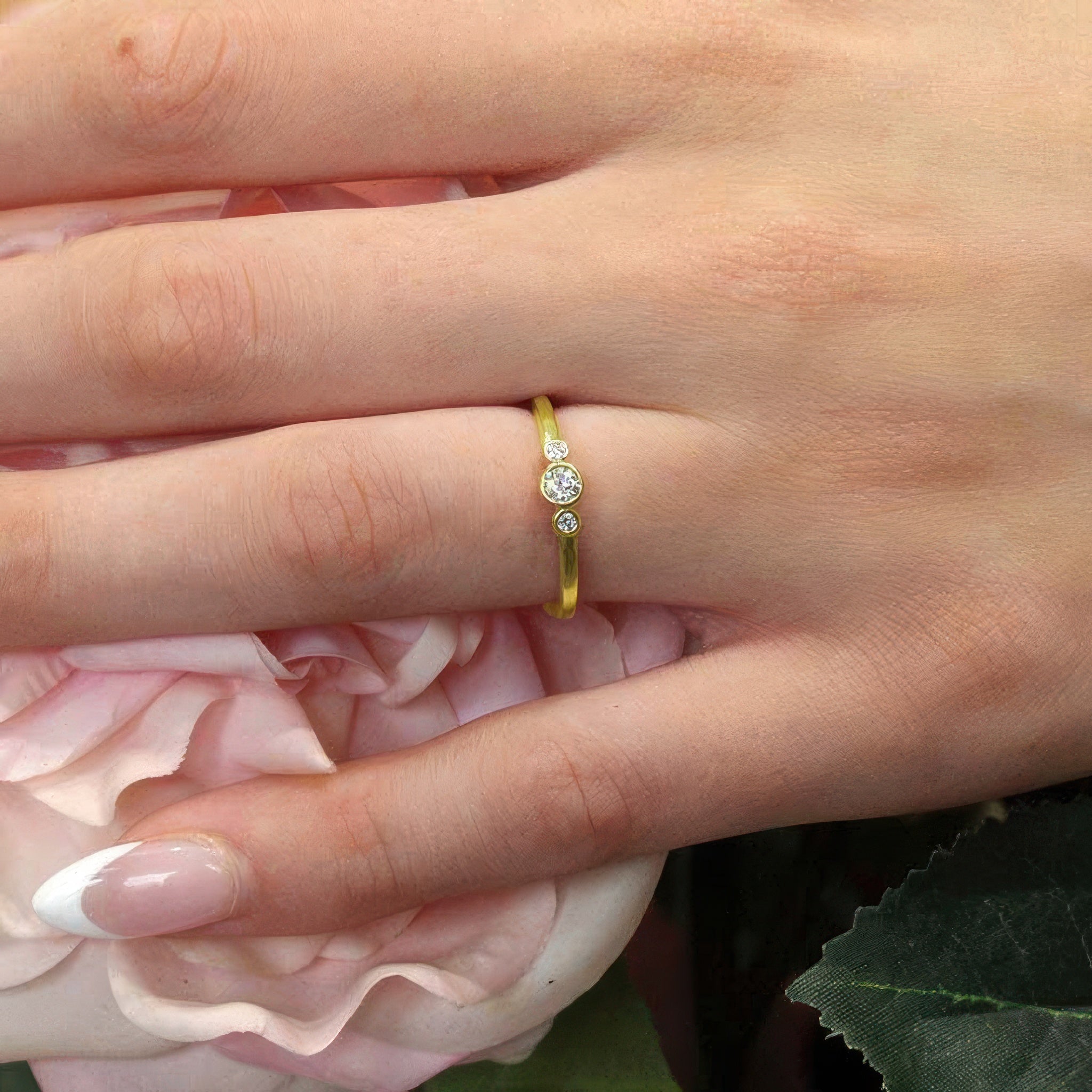 Sophia three stone promise ring in white gold, featuring a diamond center, worn on a hand with pink roses.