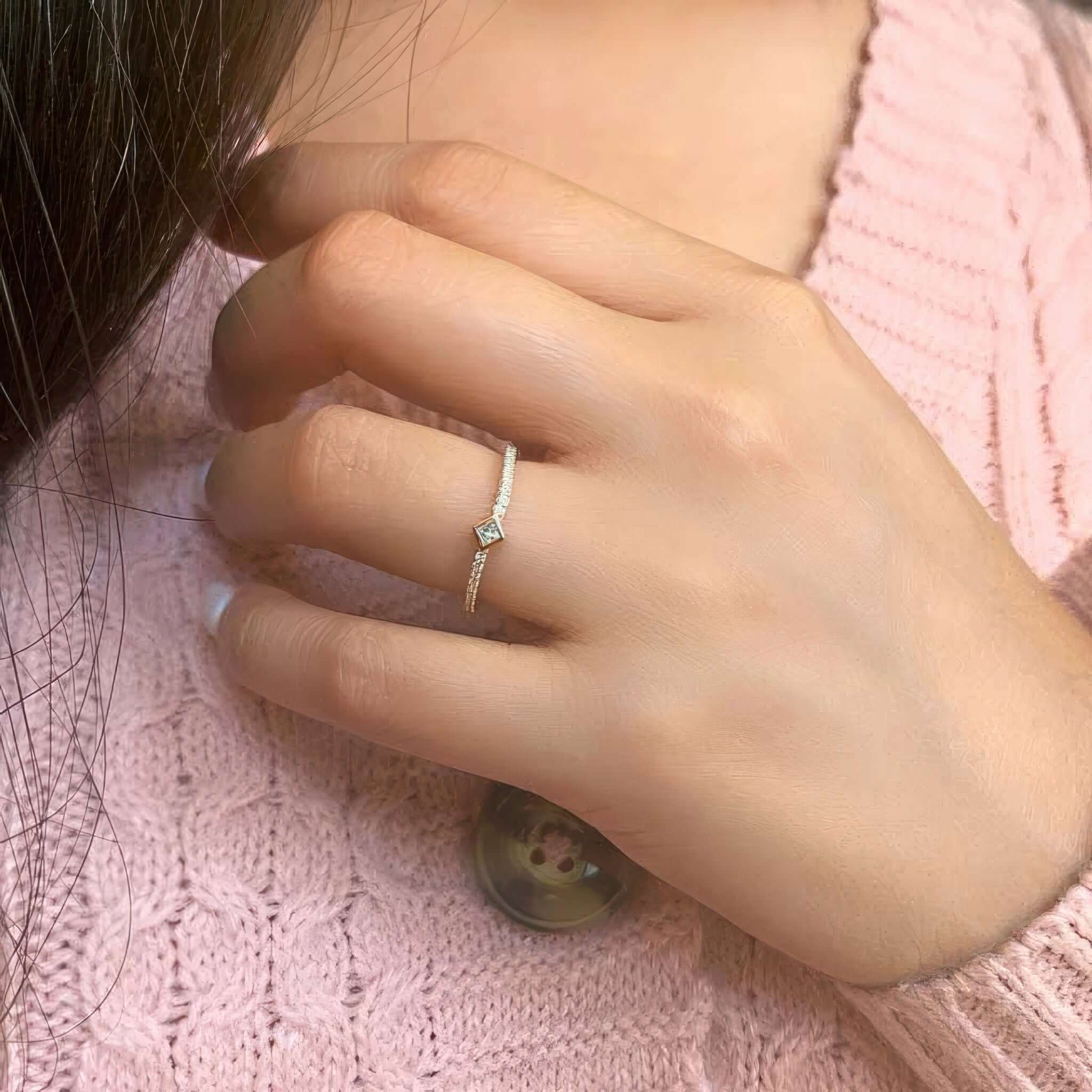 Close-up of a hand wearing the Abi Curved Princess Cut Diamond Promise Ring on a pink sweater.