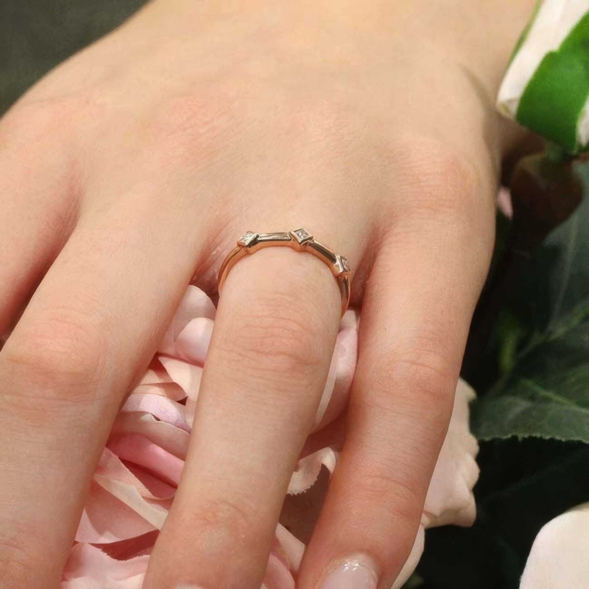 Mila Three Stone Princess Cut Promise Ring showcased on a hand with pink roses in the background, highlighting its elegant design.
