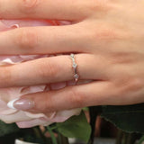 Close-up of a hand wearing a Mila three stone princess cut promise ring among pink roses.
