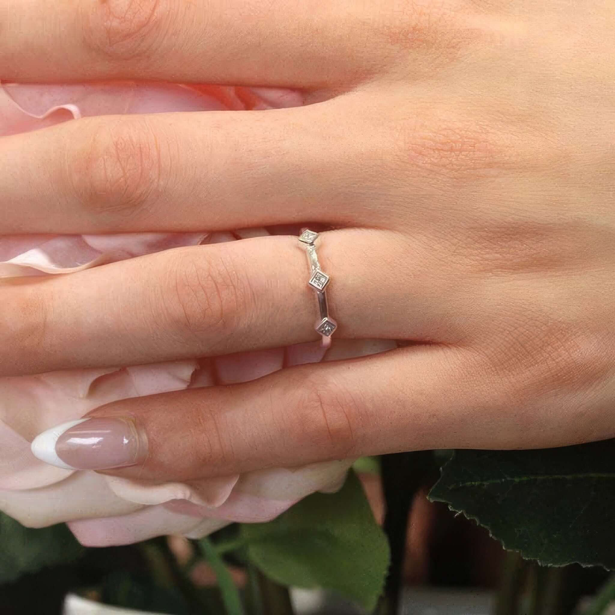 Close-up of a hand wearing a Mila three stone princess cut promise ring among pink roses.