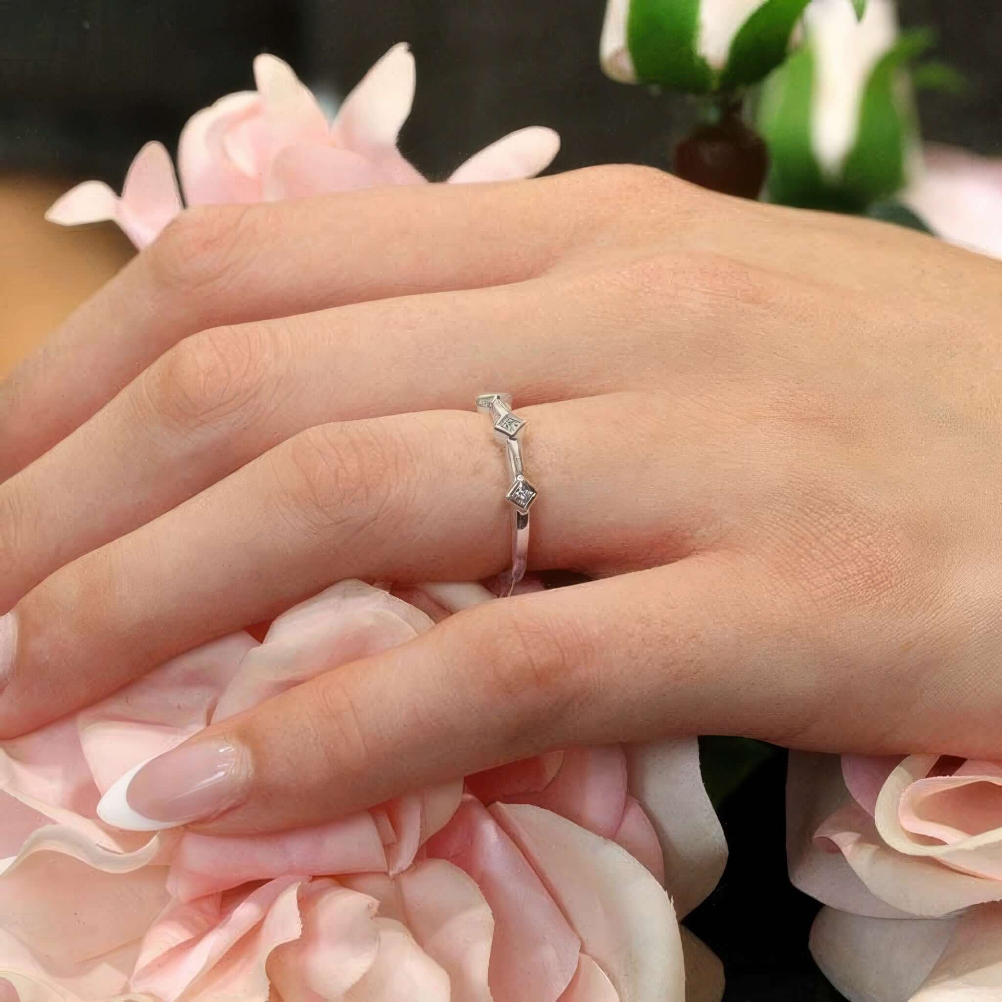 Mila three stone princess cut promise ring on hand, surrounded by pink roses, showcasing its elegant design.