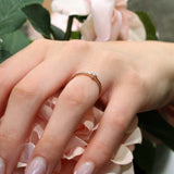 Close-up of a hand wearing the Aria Princess Cut Diamond Promise Ring with a bezel set diamond, surrounded by pink roses.