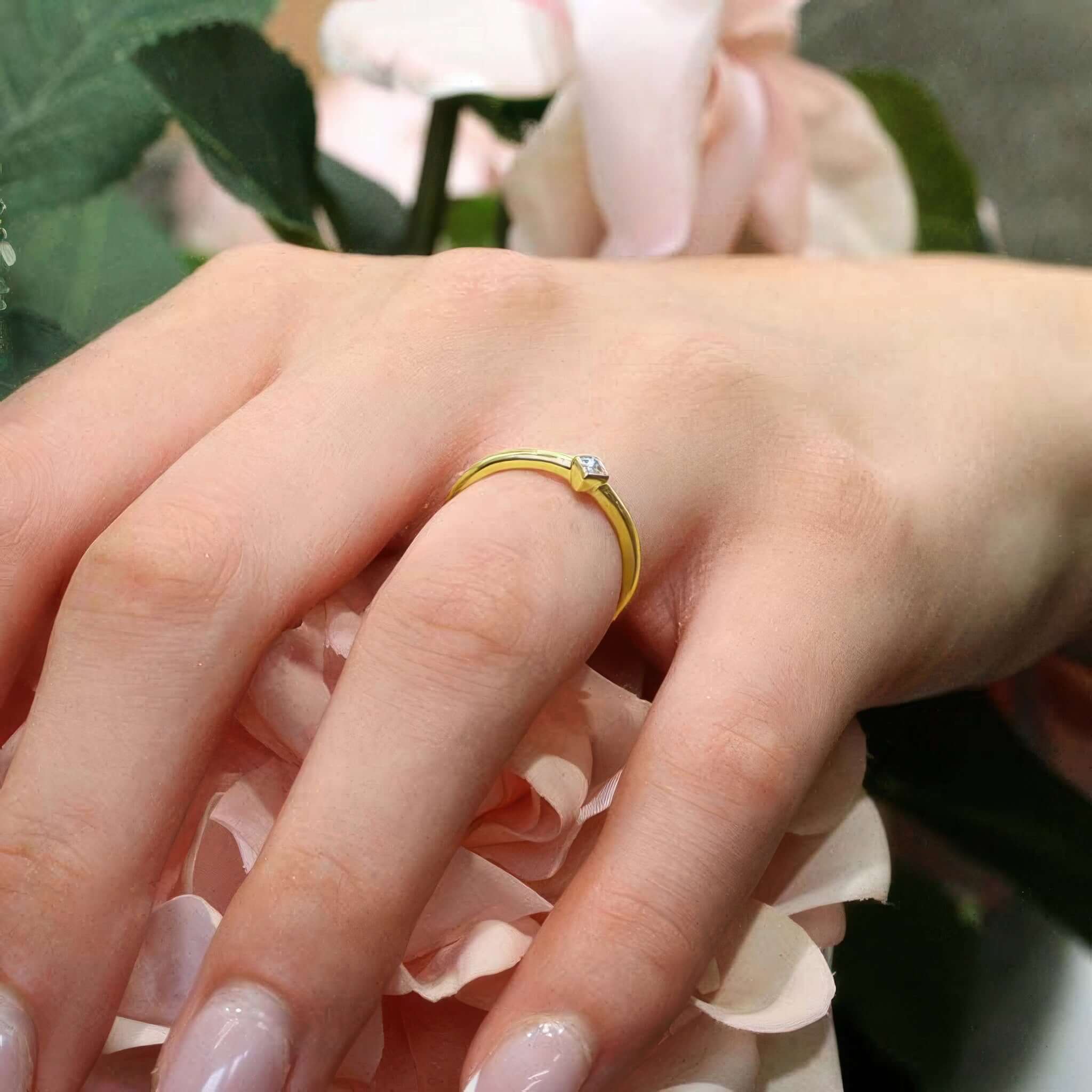 Woman's hand wearing a princess cut diamond promise ring among pink roses, showcasing timeless elegance.