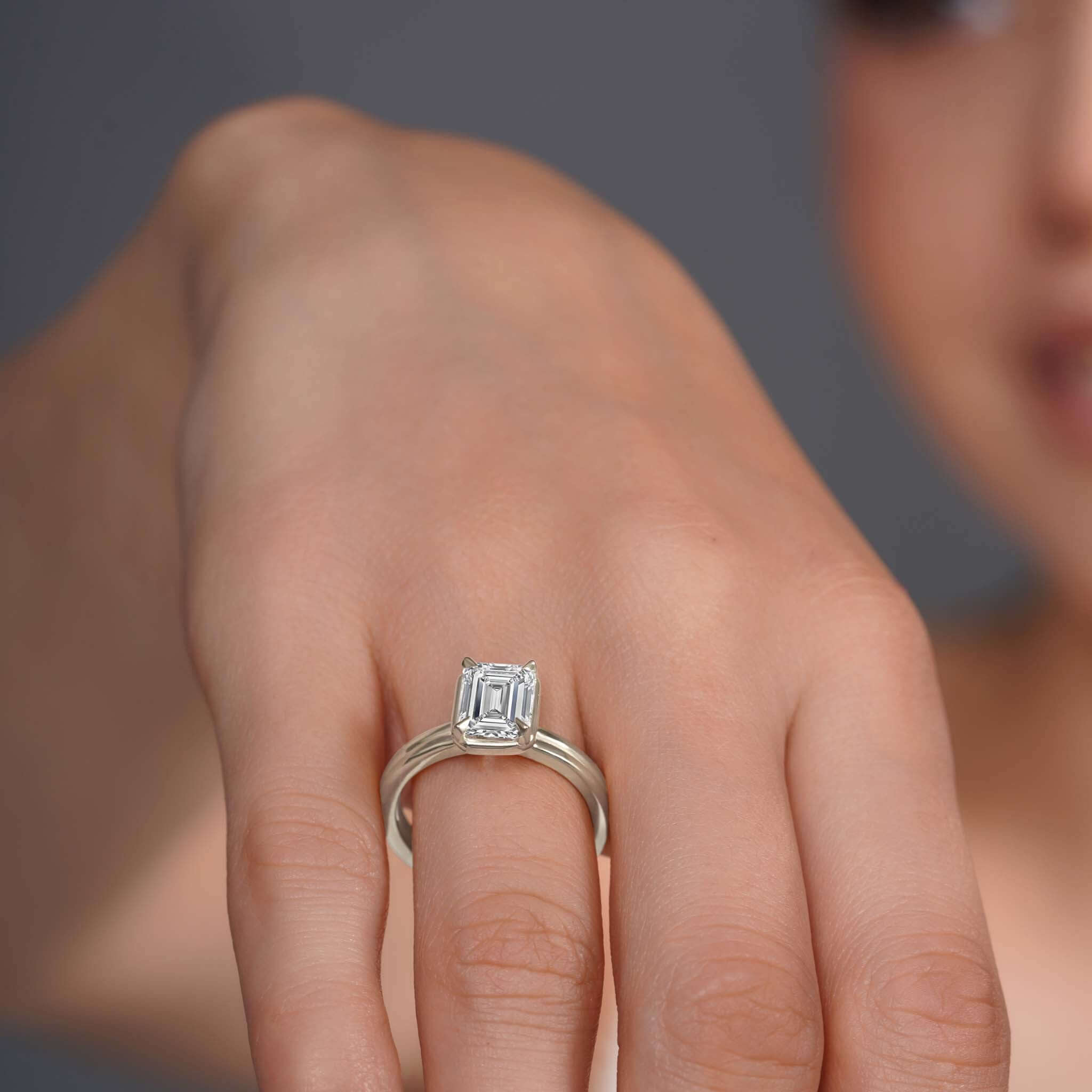Double band 2 carat emerald cut diamond solitaire ring on a model's hand, showcasing its elegance and brilliance.