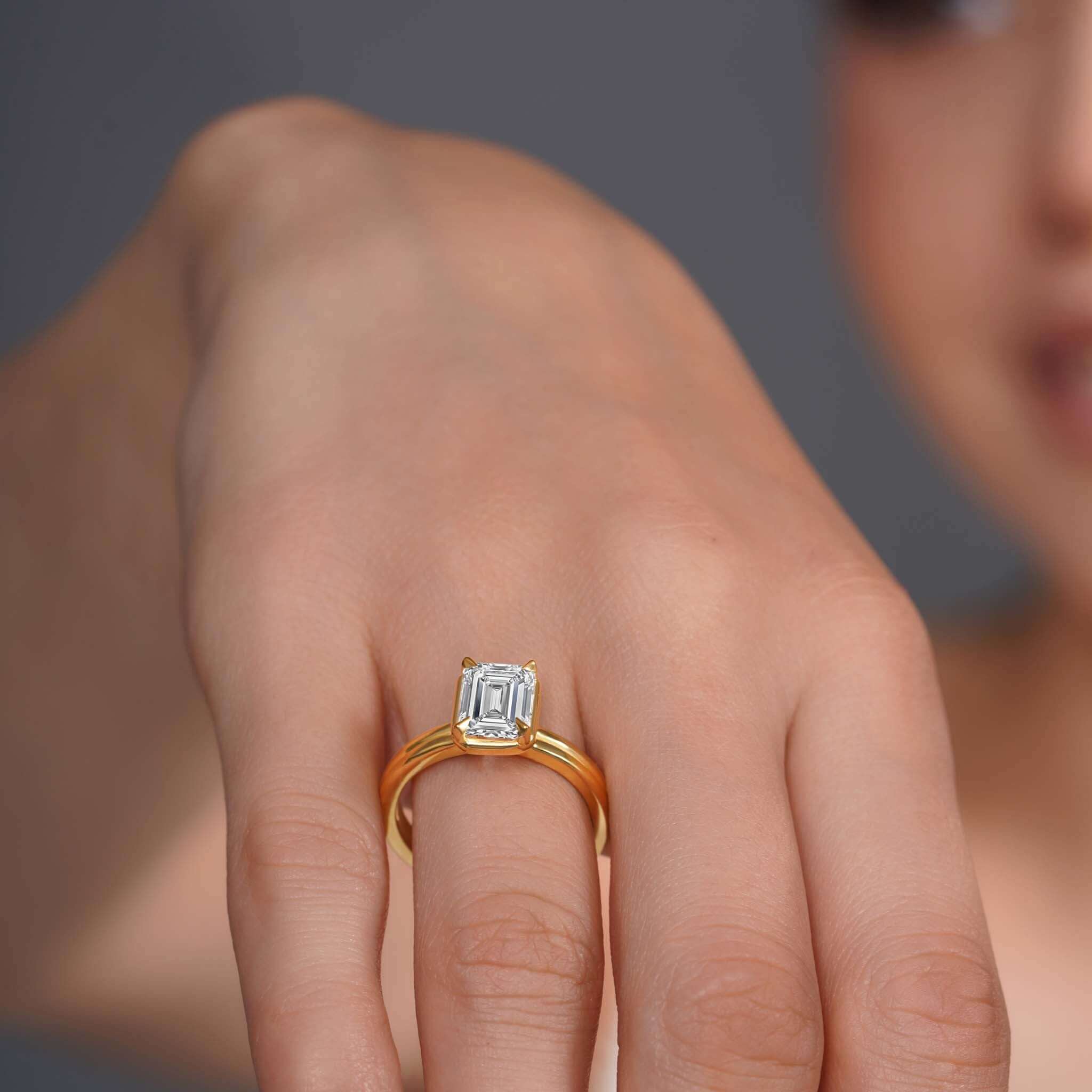 Double band 2 carat emerald cut diamond solitaire ring showcased on a model's hand with gold bands.