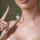 Close-up of a woman showcasing a Zodiac Necklace with a medallion pendant on a delicate chain.
