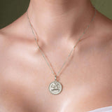 Zodiac Necklace displaying a textured medallion with a zodiac symbol, worn on a delicate chain.