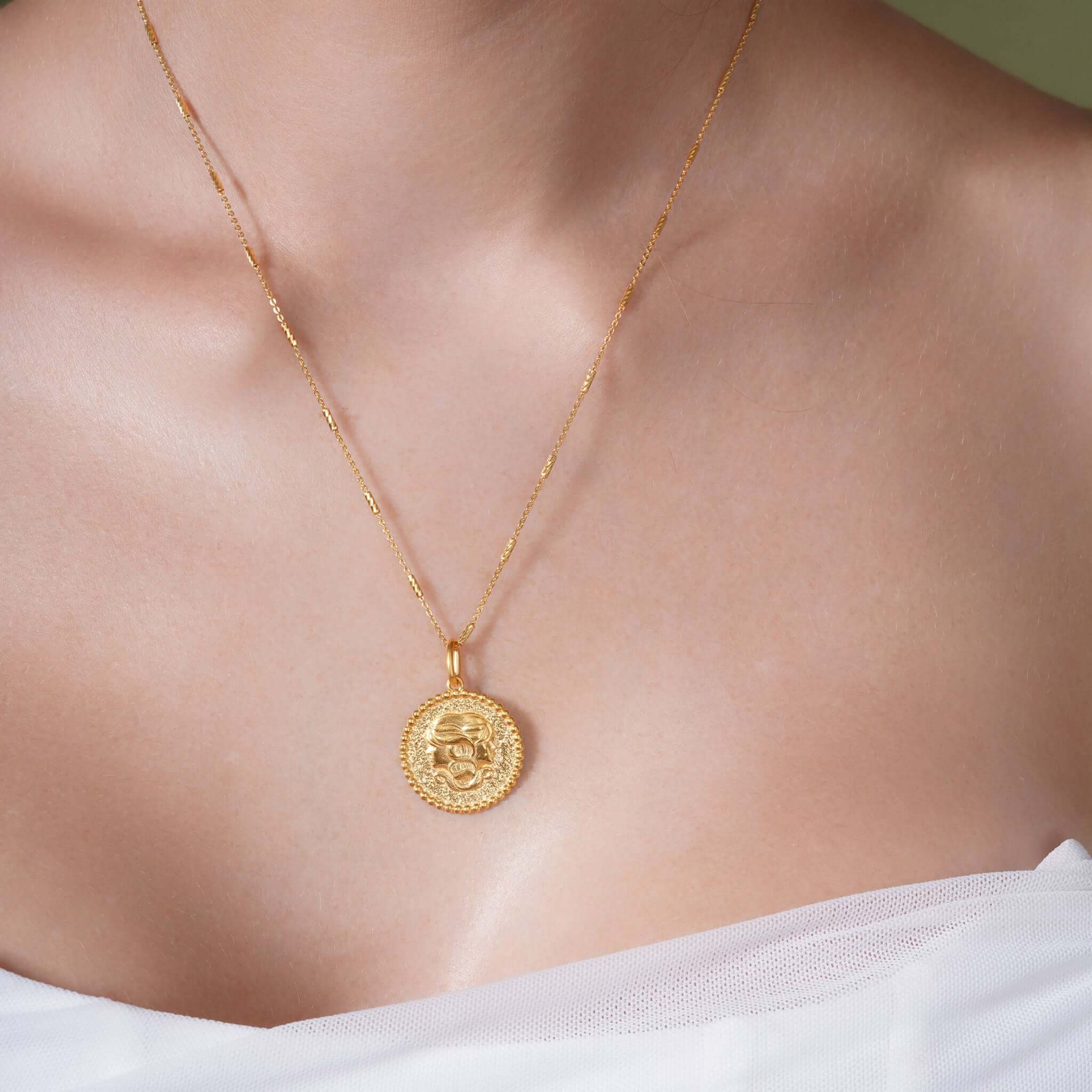 Zodiac Necklace showcasing gold medallion with zodiac symbol, worn on a sleek chain against a textured background.