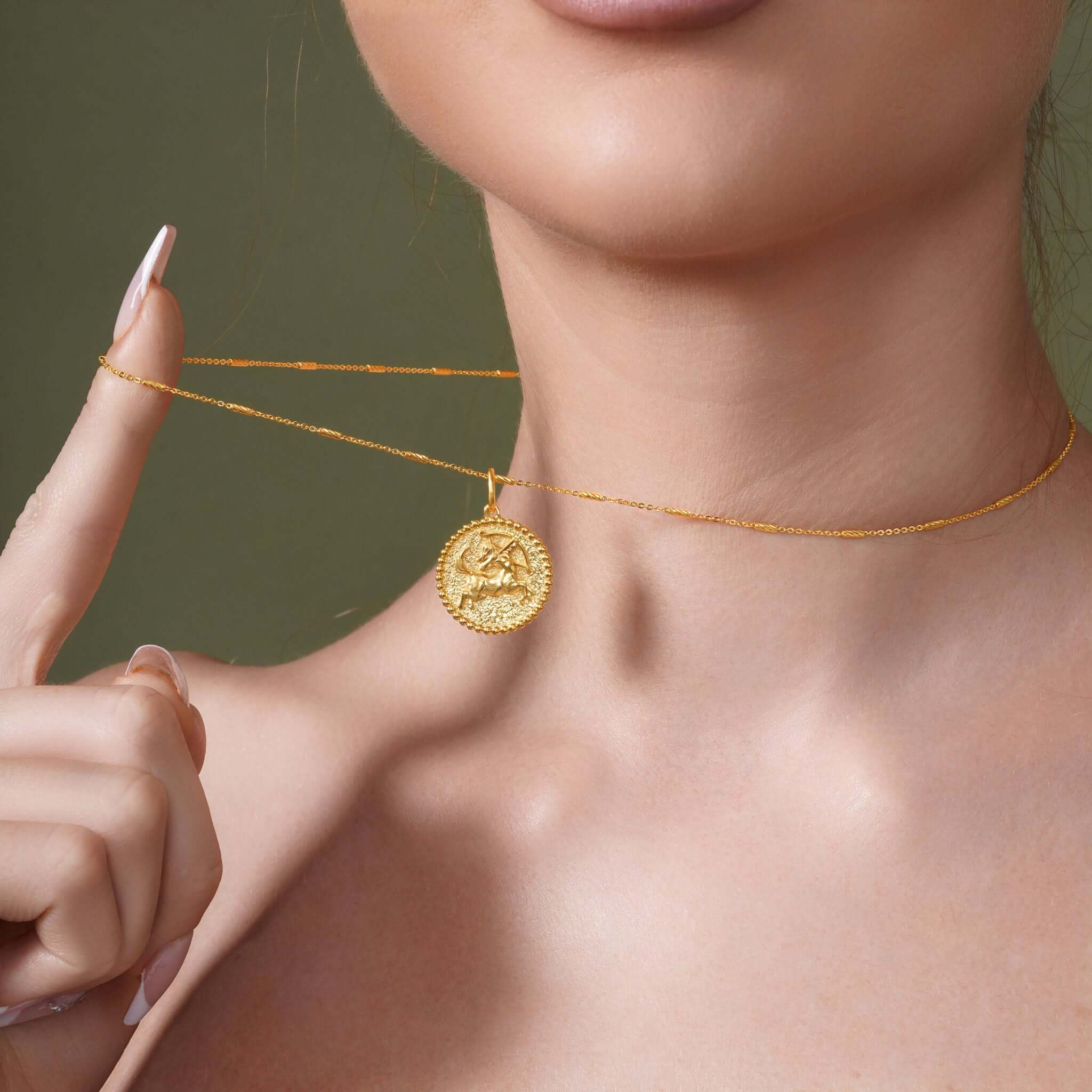Close-up of a woman showcasing a gold Zodiac Necklace medallion on a delicate chain.