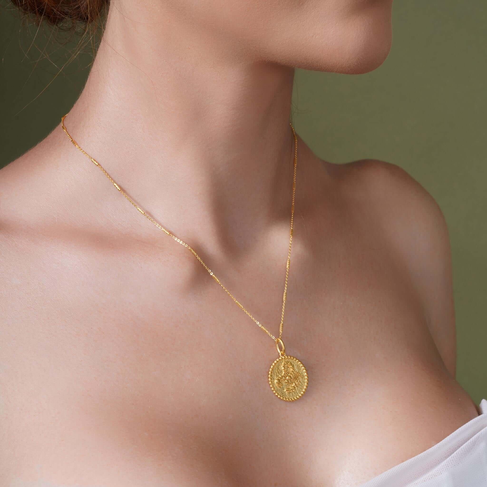 Close-up of a woman wearing a gold Zodiac Necklace with a medallion pendant.