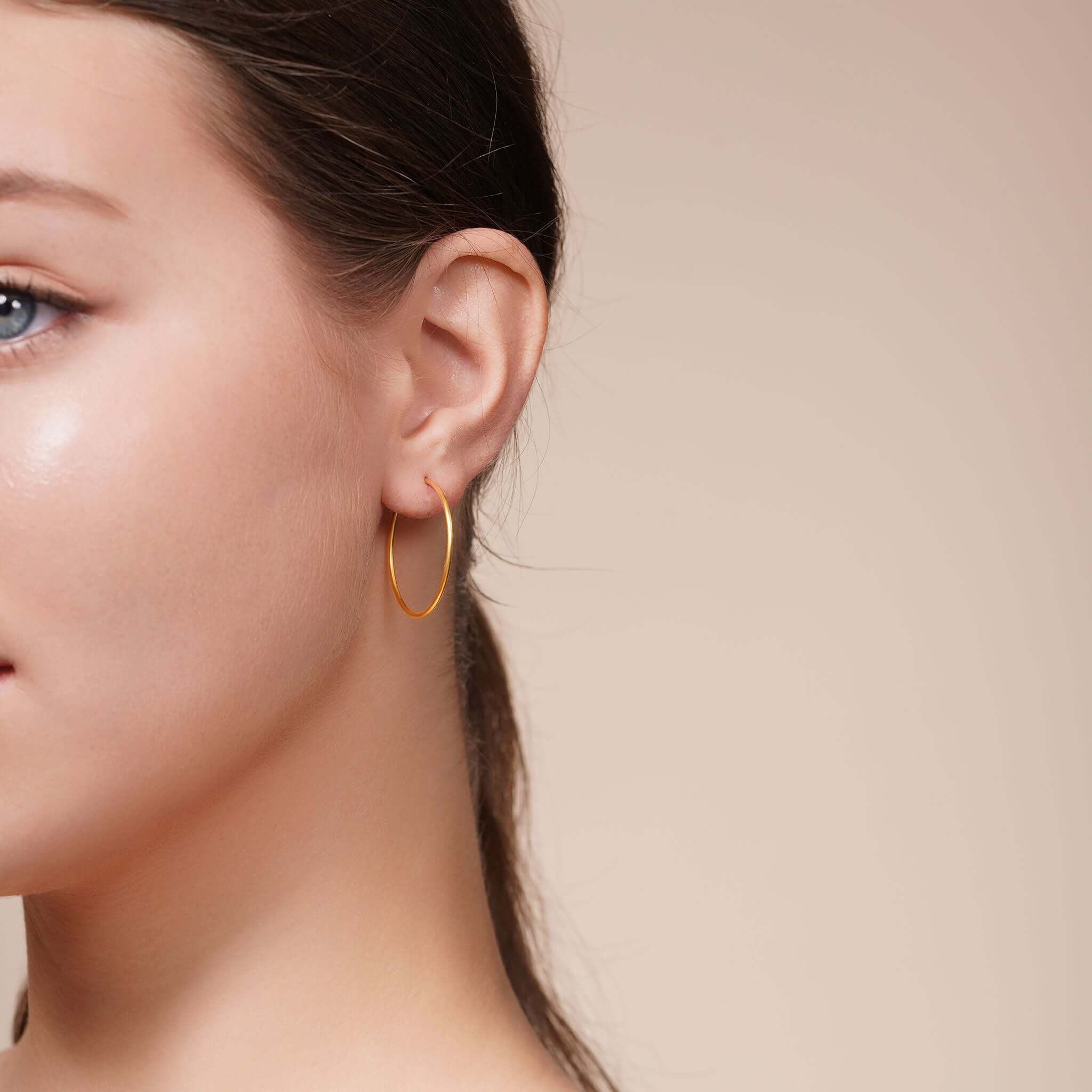 Close-up of a model wearing Gold Endless Hoop Earrings, showcasing their seamless design and shine.