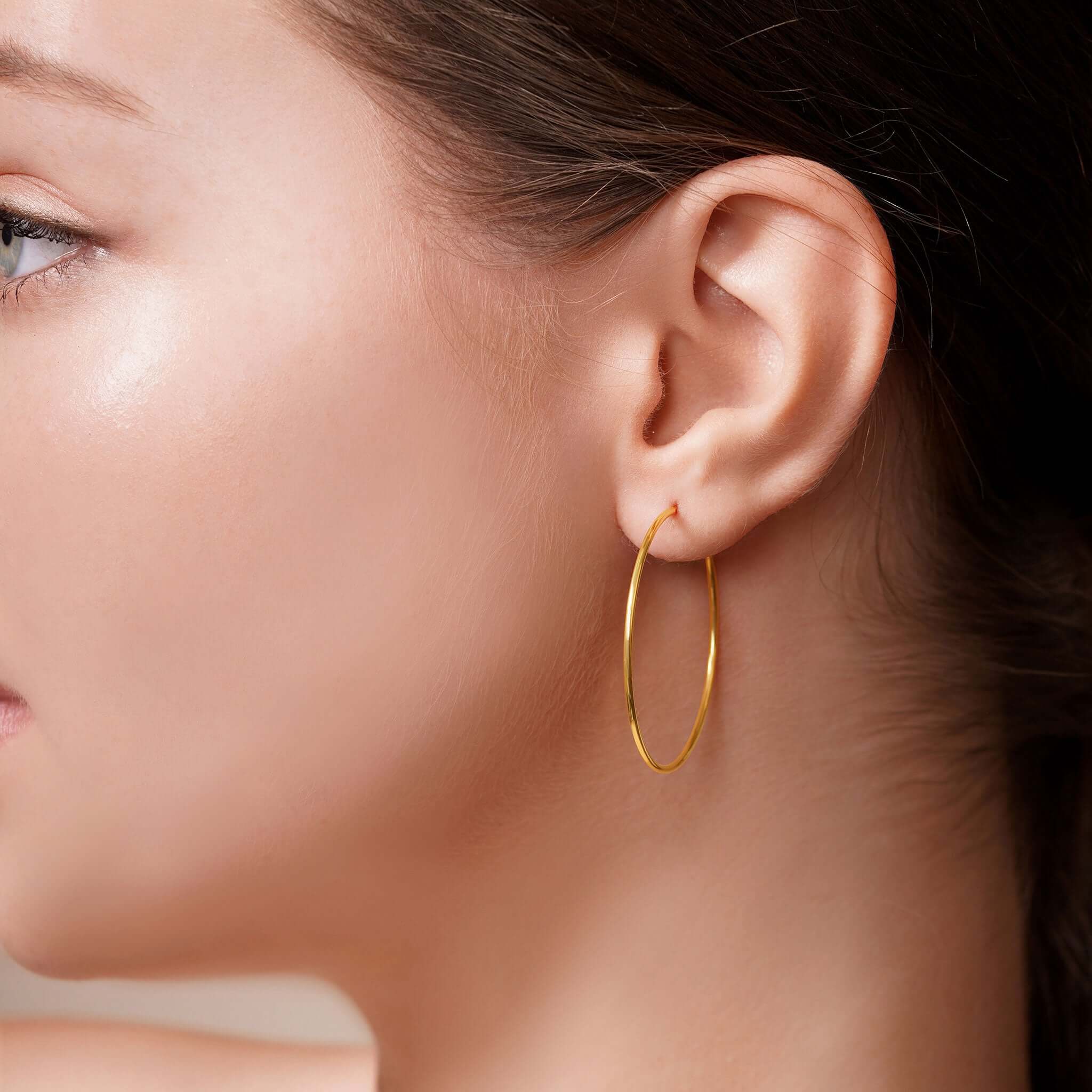 Profile view of a woman wearing Gold Endless Hoop Earrings, showcasing their timeless and elegant design.