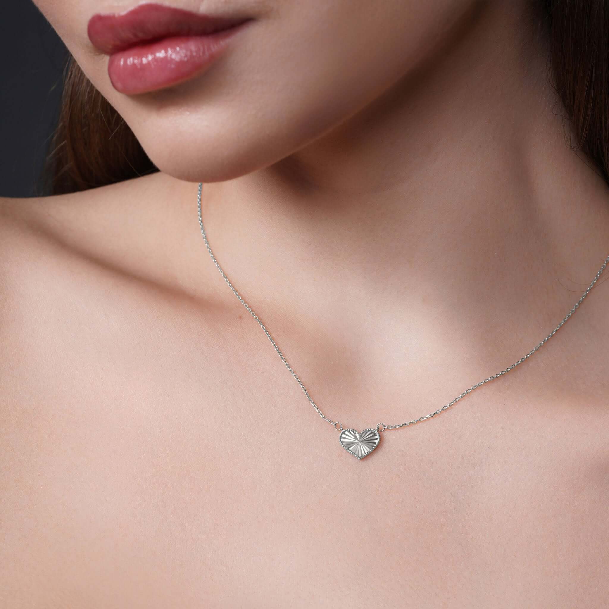Model wearing an Engraved Heart Necklace in silver, showcasing the textured heart pendant on display.