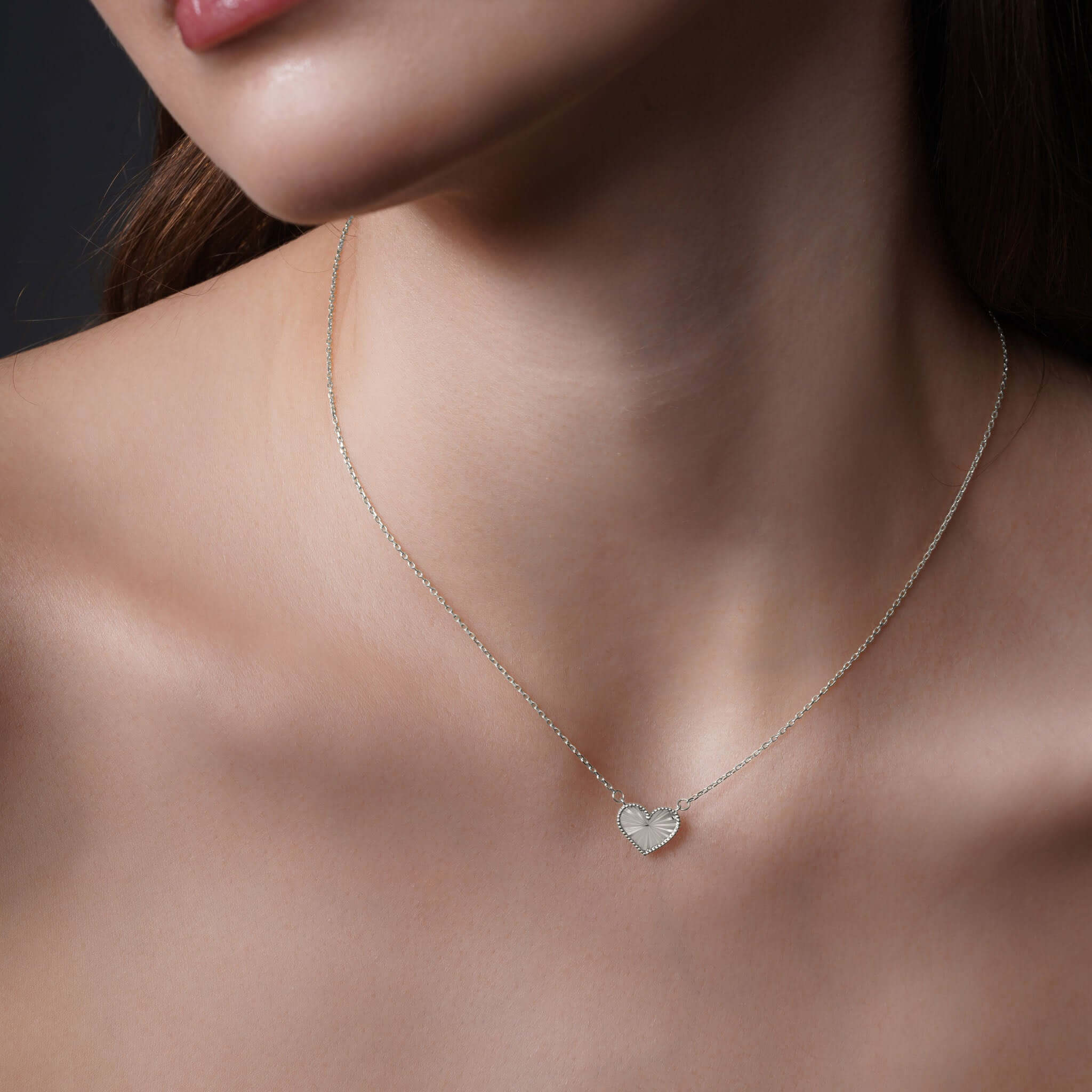 Close-up of a woman wearing an Engraved Heart Necklace in silver, showcasing its intricate design and elegance.
