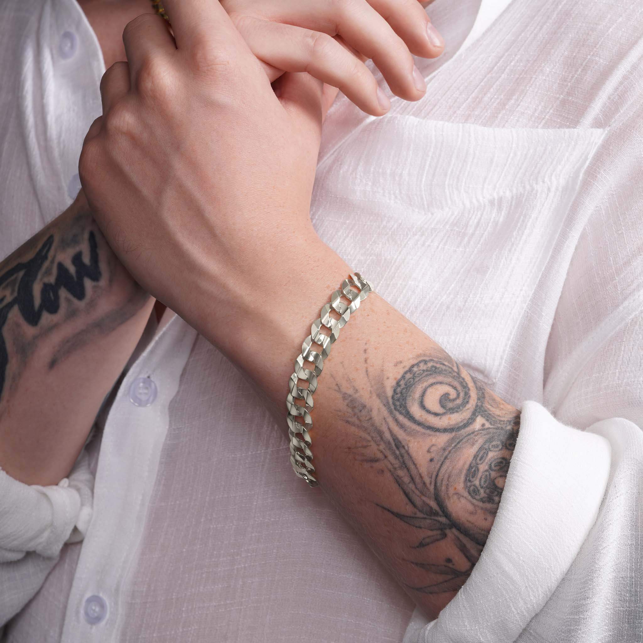 Men's solid gold curb bracelet showcasing a classic design, worn on a tattooed wrist with a white shirt.