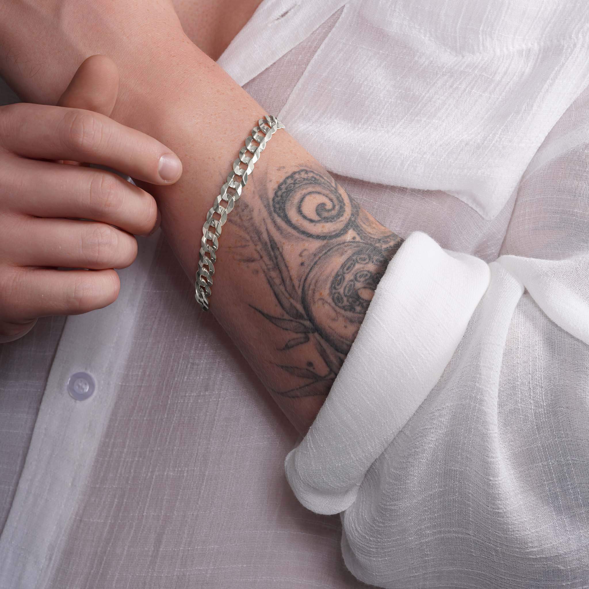 Men's solid gold curb bracelet shown on a wrist with a tattoo, showcasing elegant design and craftsmanship.