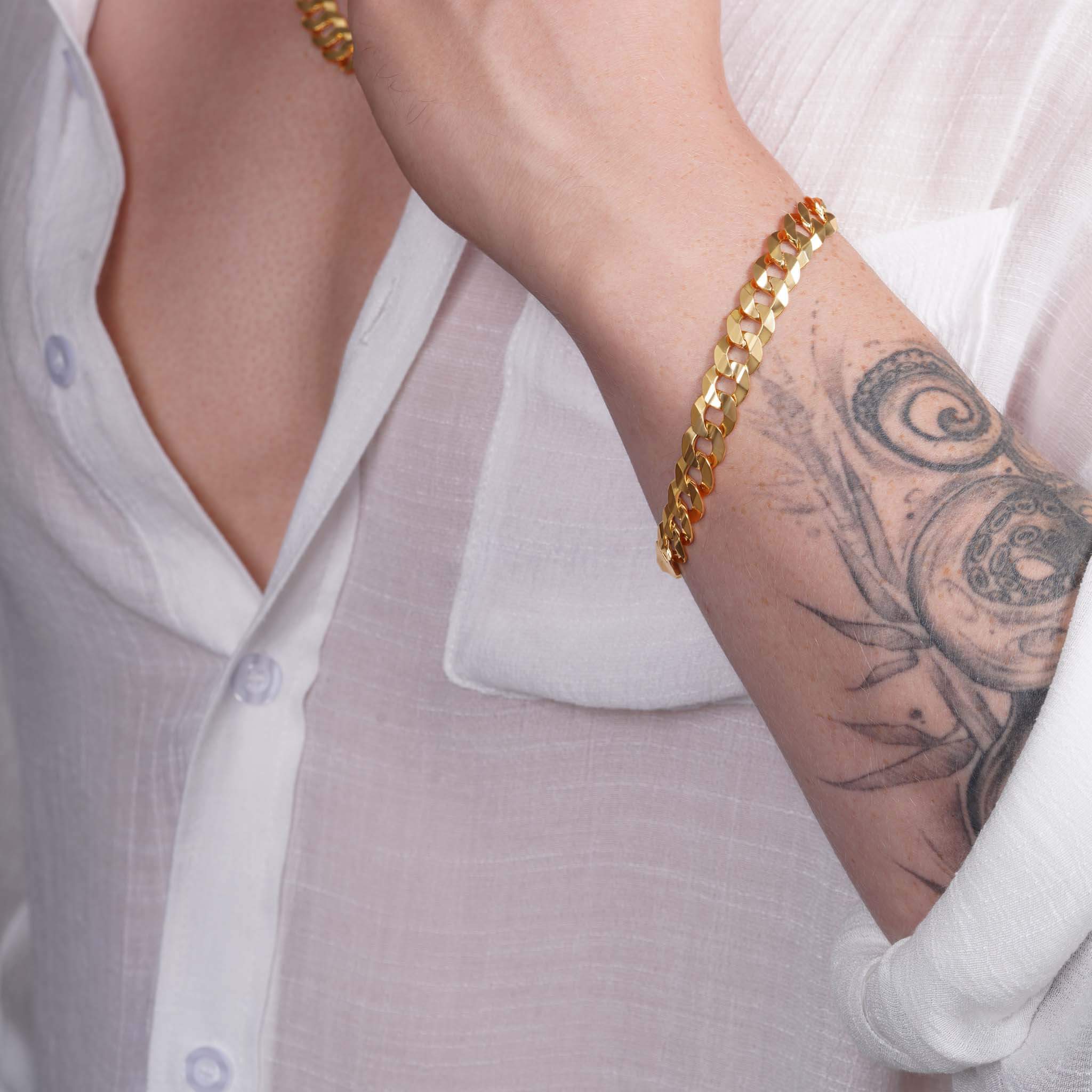 Men's solid gold curb bracelet in 14K yellow gold worn on wrist with tattoo, showcasing stylish elegance.