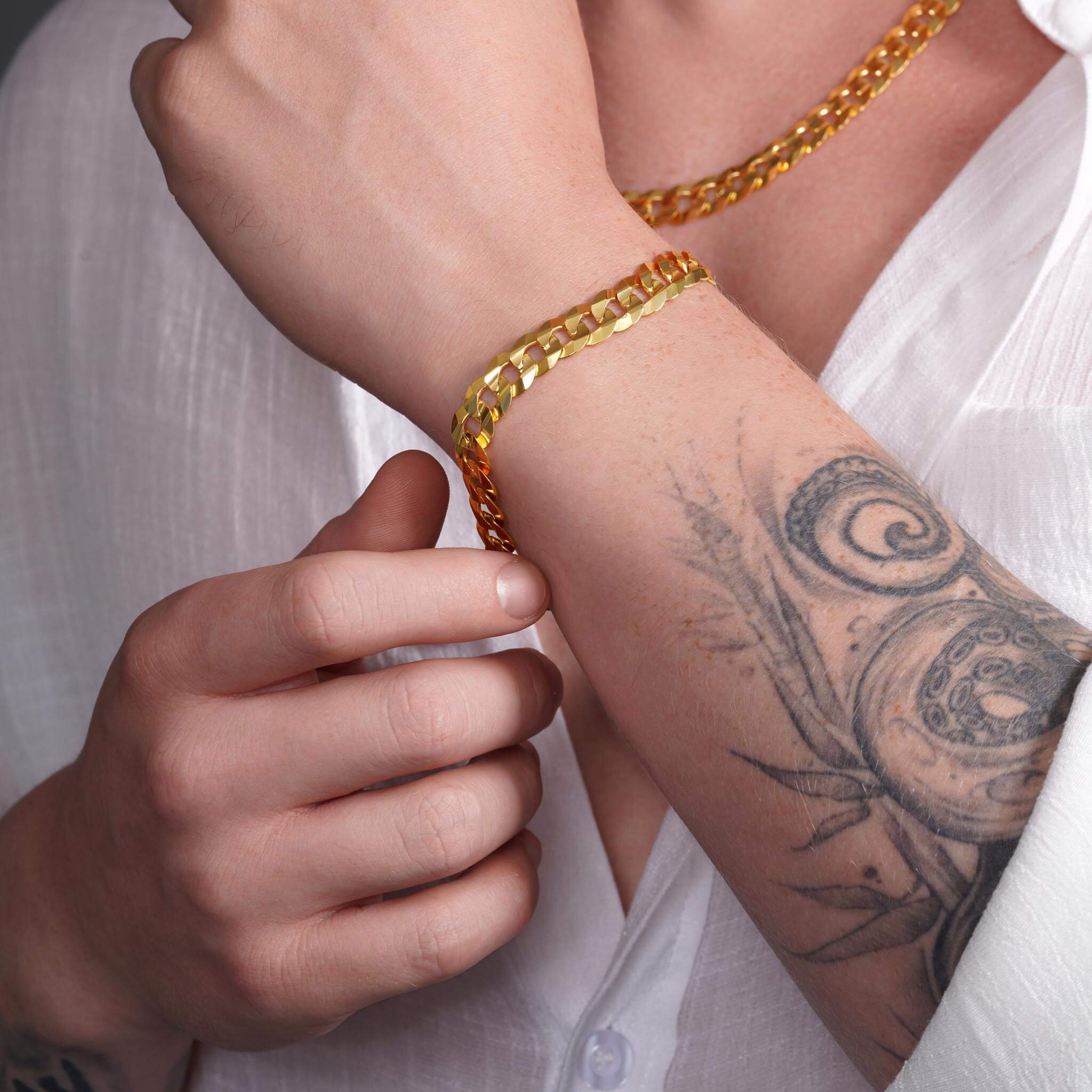 Men's solid gold curb bracelet in 14K yellow gold, showcasing a bold design and expert craftsmanship on a tattooed wrist.