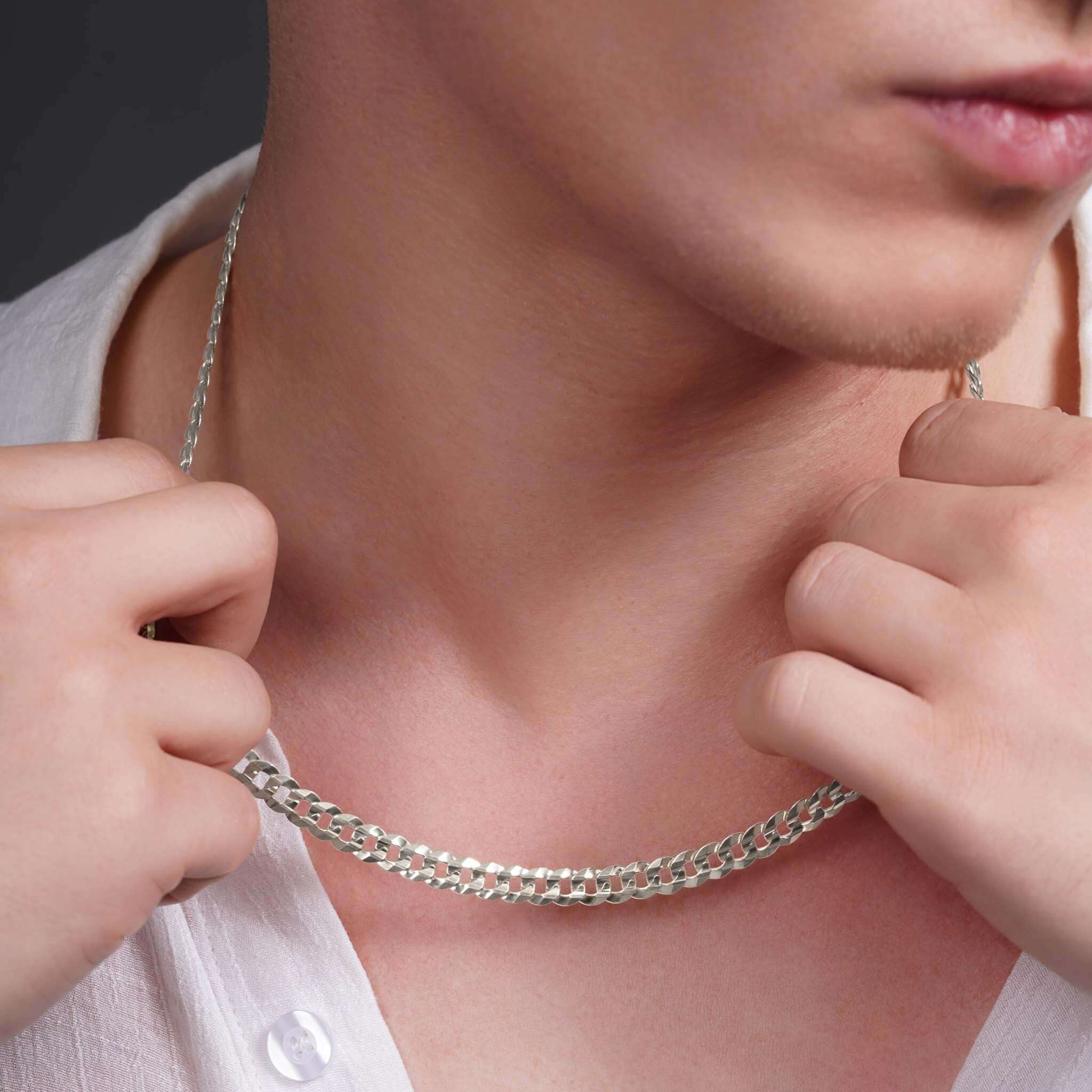 Close-up of a man adjusting a solid gold curb chain necklace, showcasing its interlocking links and elegant design.