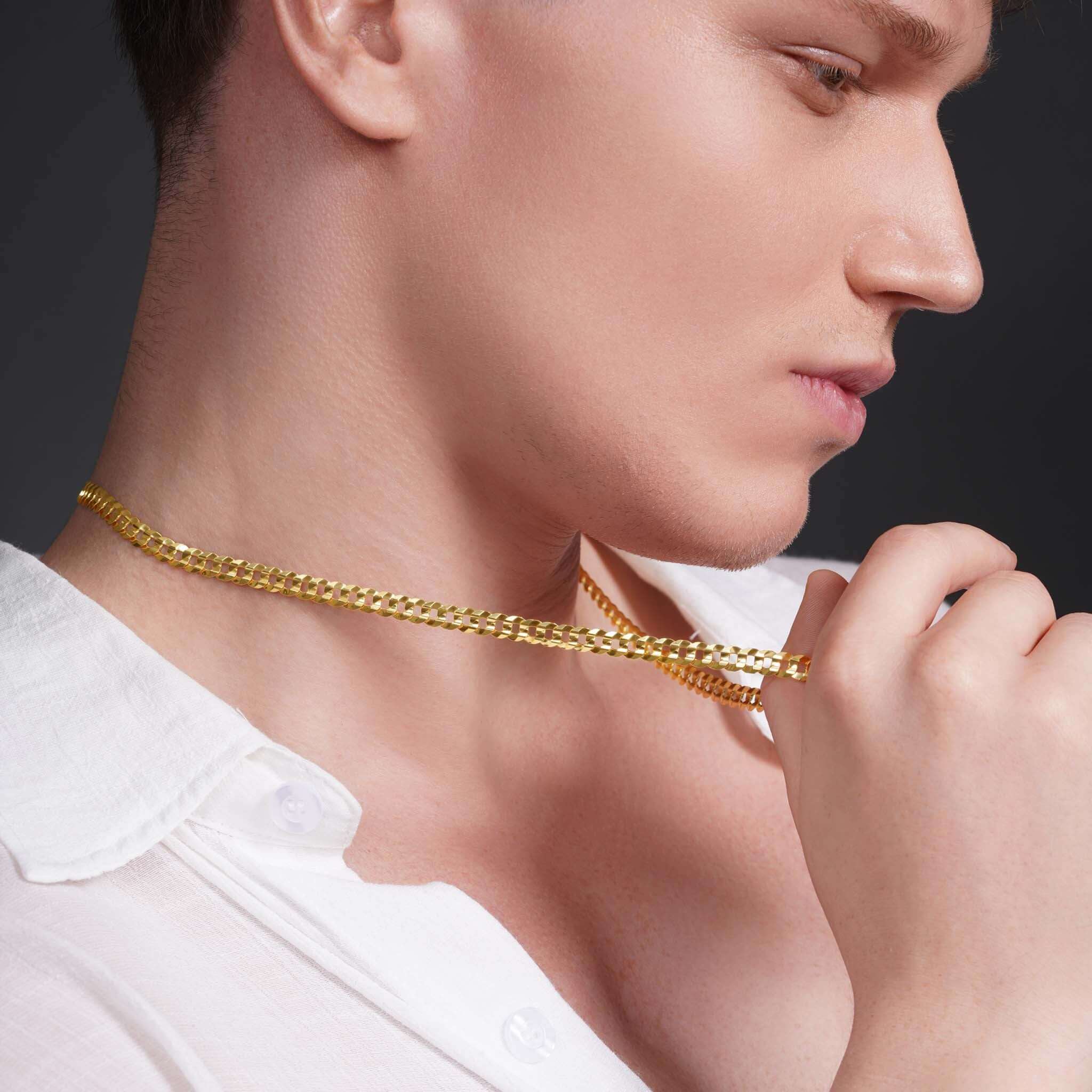 Stylish man holding a 14k solid gold curb chain, showcasing its shine and elegance against his skin.