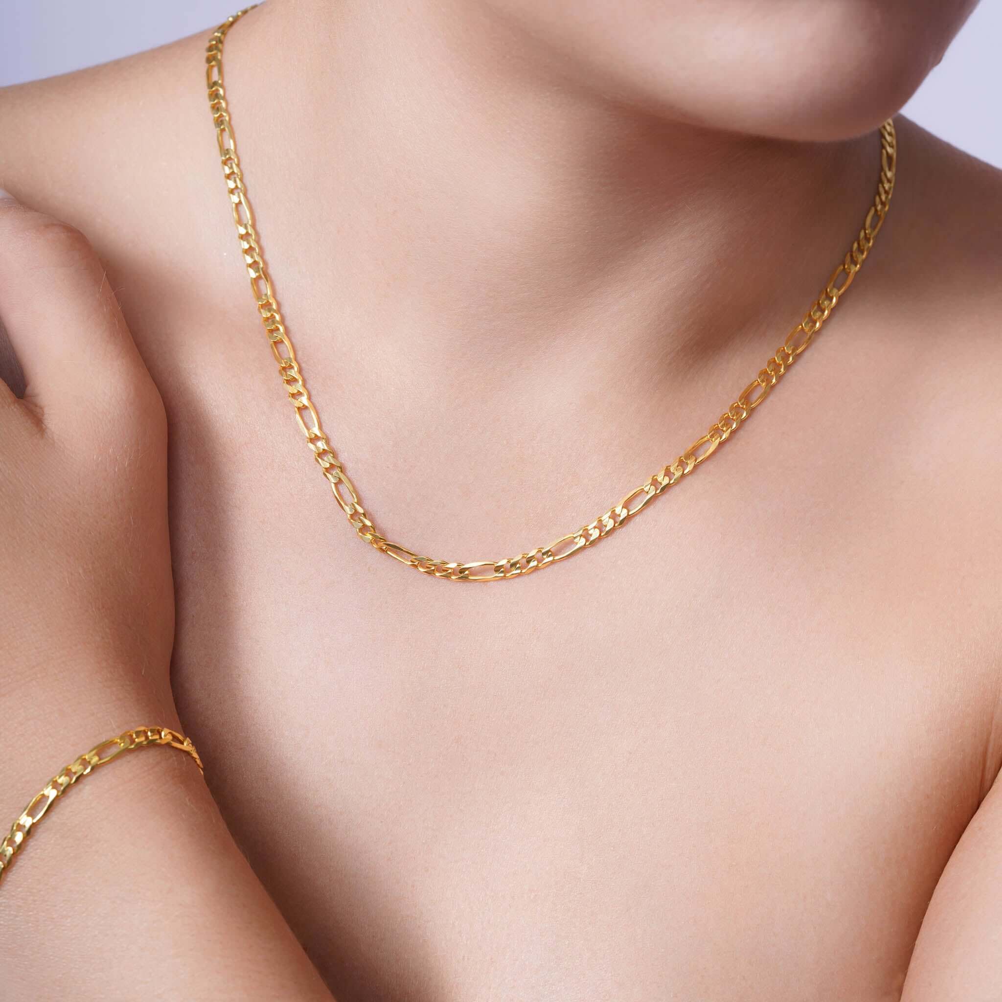 Elegant woman wearing a Figaro Gold Chain and matching bracelet, showcasing timeless gold jewelry design.