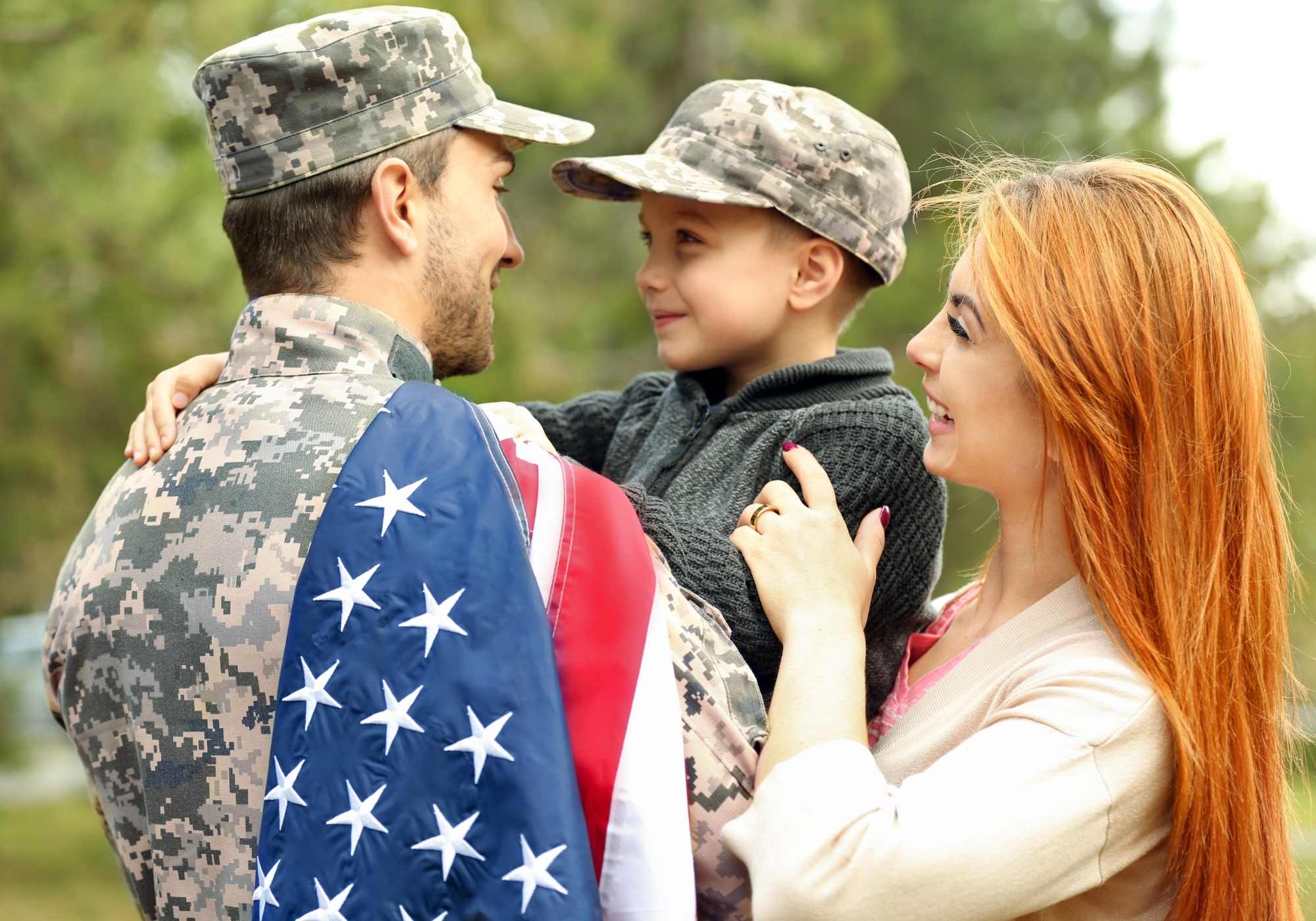 Man in military uniform with child and woman outdoors, holding American flag