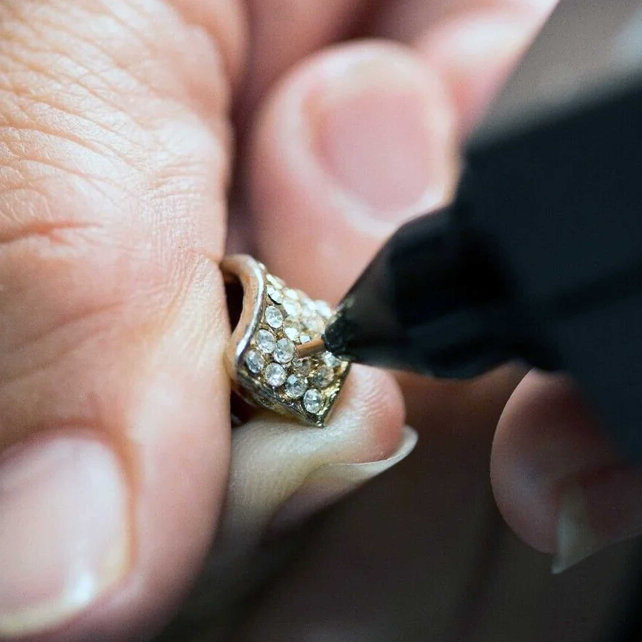Close-up of a diamond tester being used on a ring to verify the authenticity of diamonds in a jewelry piece.