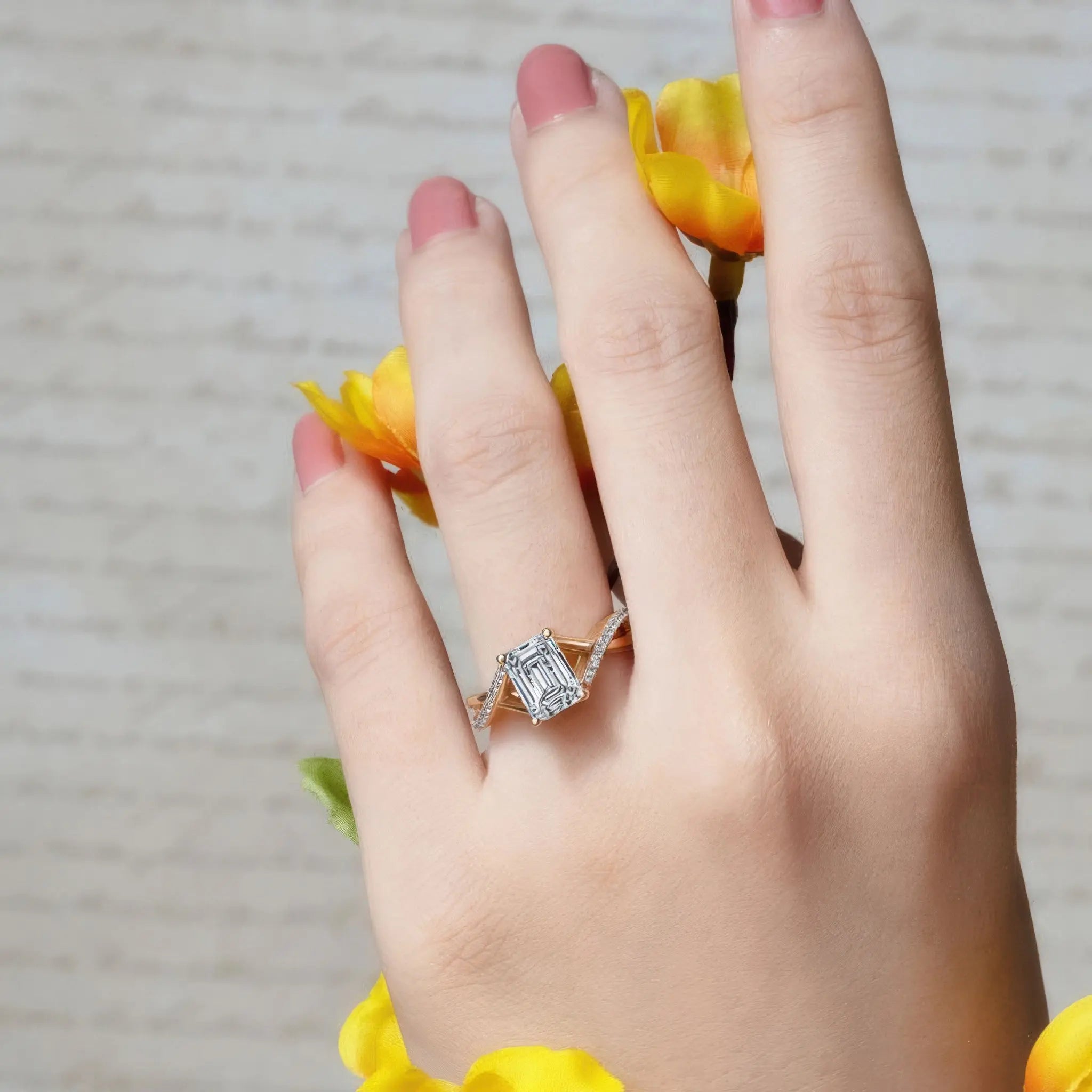 Elegant hand wearing a big diamond ring with an emerald cut stone, styled with yellow flowers.