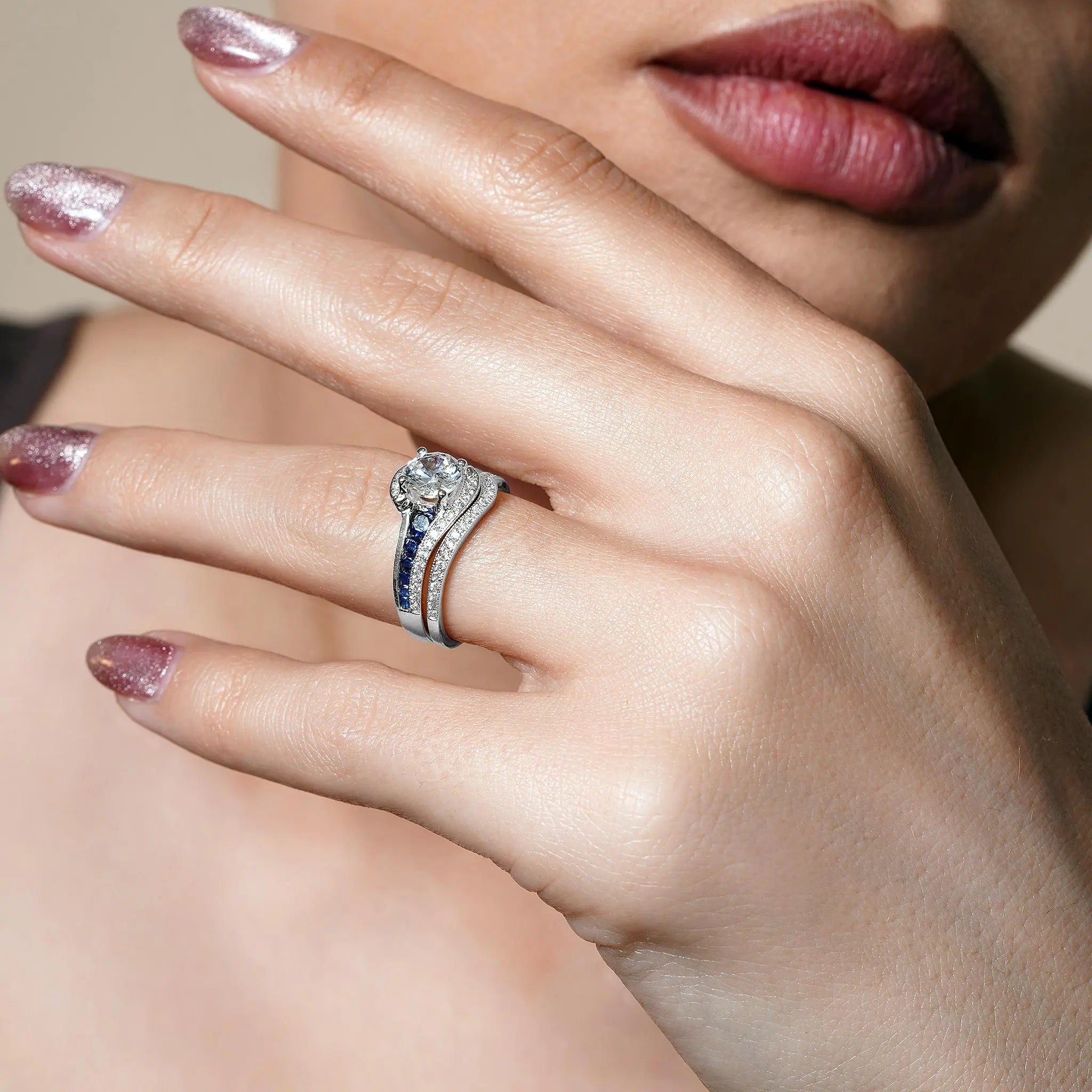 Close-up of a hand wearing a blue sapphire wedding set, featuring a diamond engagement ring and matching band.