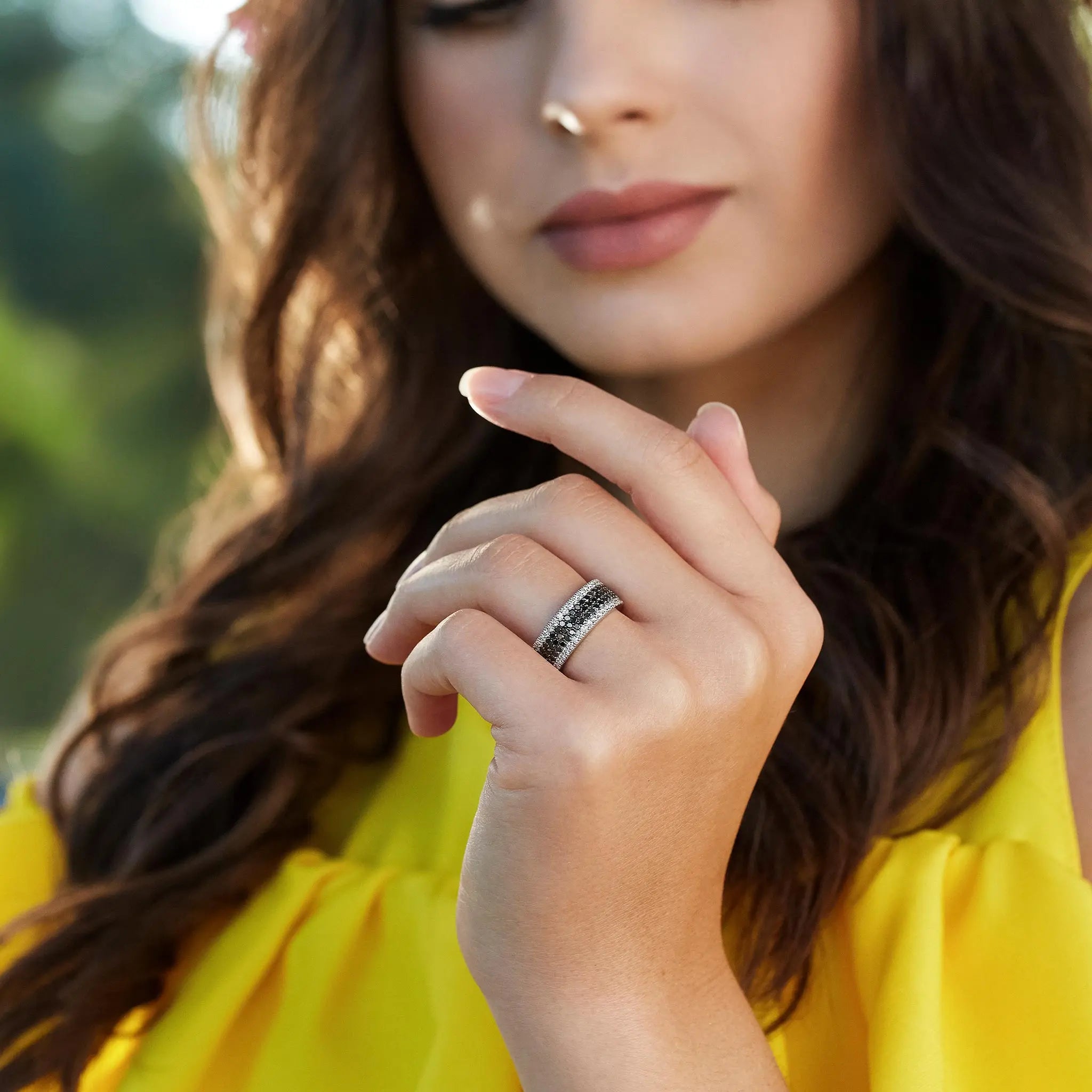 Close-up of a woman's hand wearing a black diamond wedding band, showcasing elegance against a vibrant yellow top.