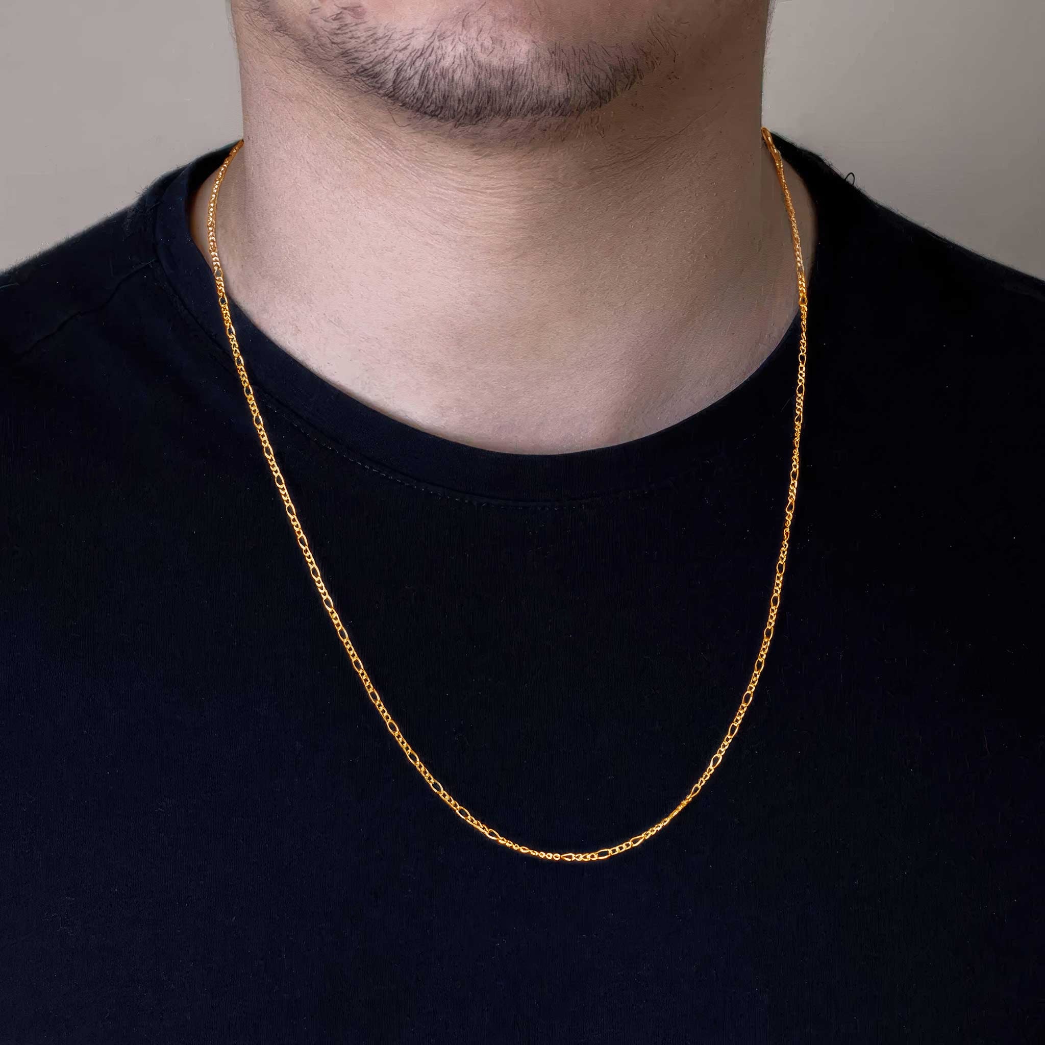 Gold figaro chain necklace worn by a person on a plain background