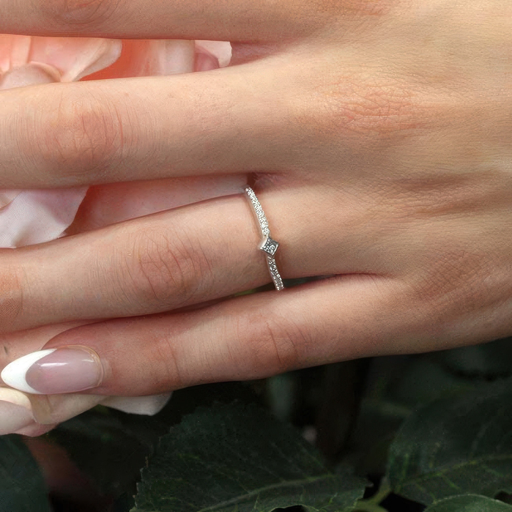 Close-up of a hand wearing an Abi curved princess cut diamond promise ring with bezel set and shared prong set diamonds.