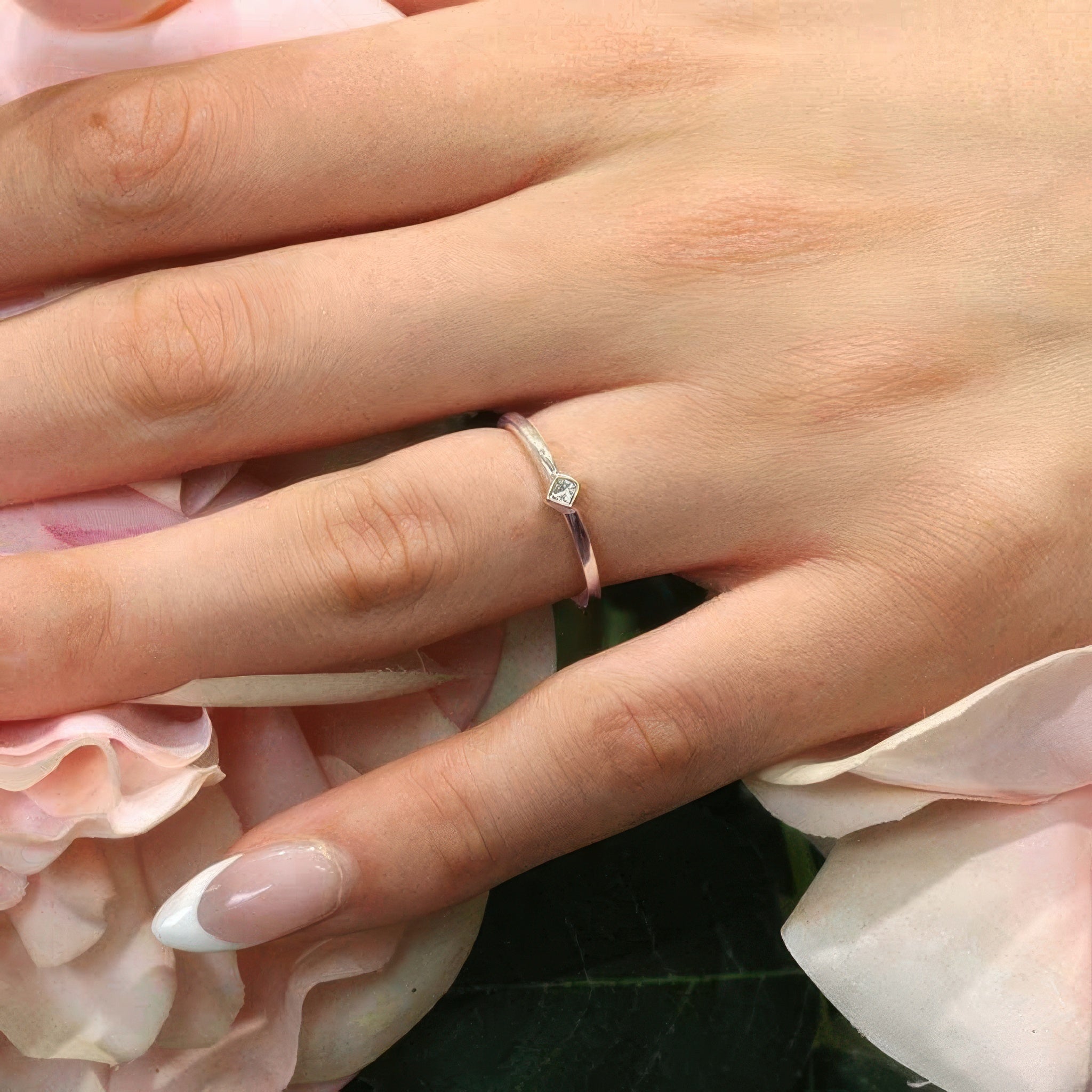 Hand displaying a classic princess cut diamond promise ring on a bed of pink roses.