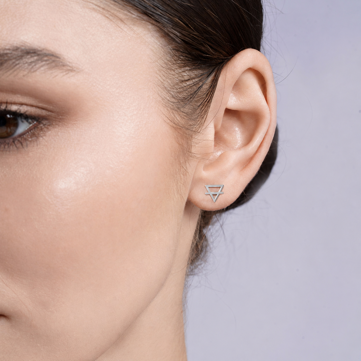 Close-up of an ear wearing a silver earth element alchemy stud earring against a neutral background