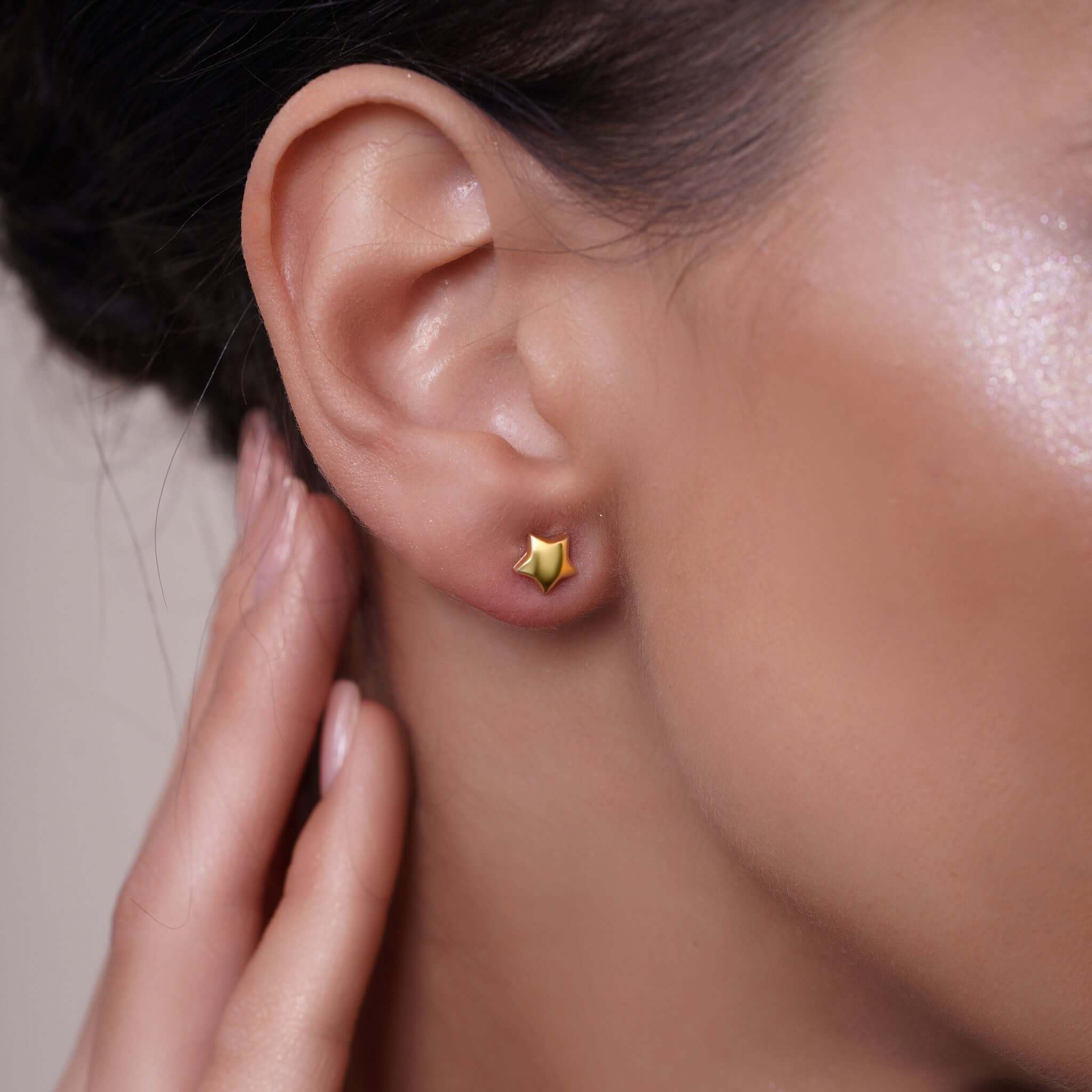 Close-up of an ear wearing a 14k gold star-shaped earring with a blurred background