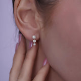 Close-up of a person wearing white gold stud earrings containing 3  dangling diamonds with a blurred background