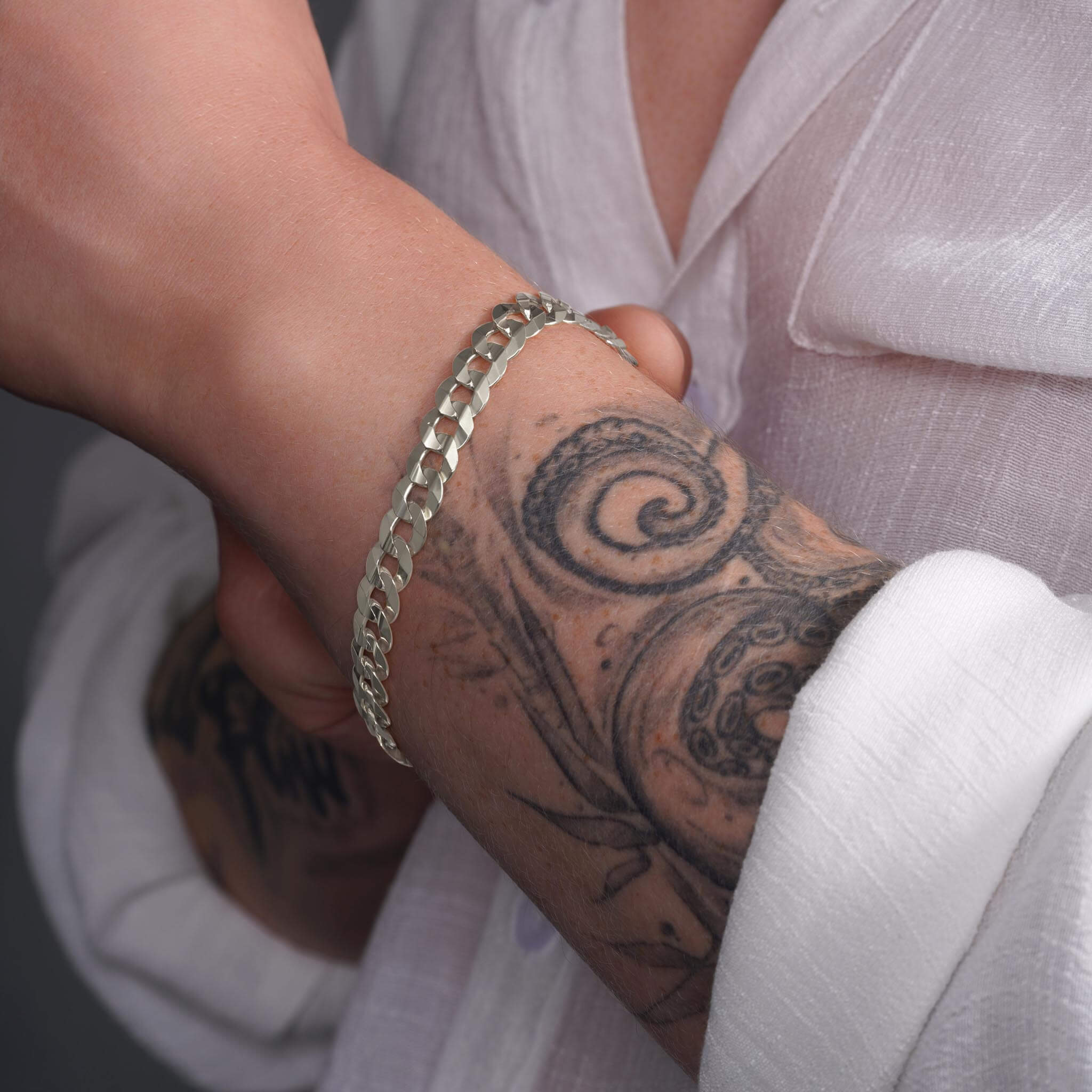 Men's solid gold curb bracelet featured on a tattooed wrist, showcasing its elegant design and durable craftsmanship.