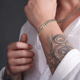 Men's solid gold curb bracelet worn on a tattooed wrist, showcasing classic design and elegance.
