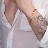 Men's solid gold curb bracelet in 14K yellow gold worn on wrist with tattoo, showcasing stylish elegance.