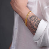 Men's solid gold curb bracelet showcased on a tattooed wrist, highlighting its classic design and luxurious craftsmanship.