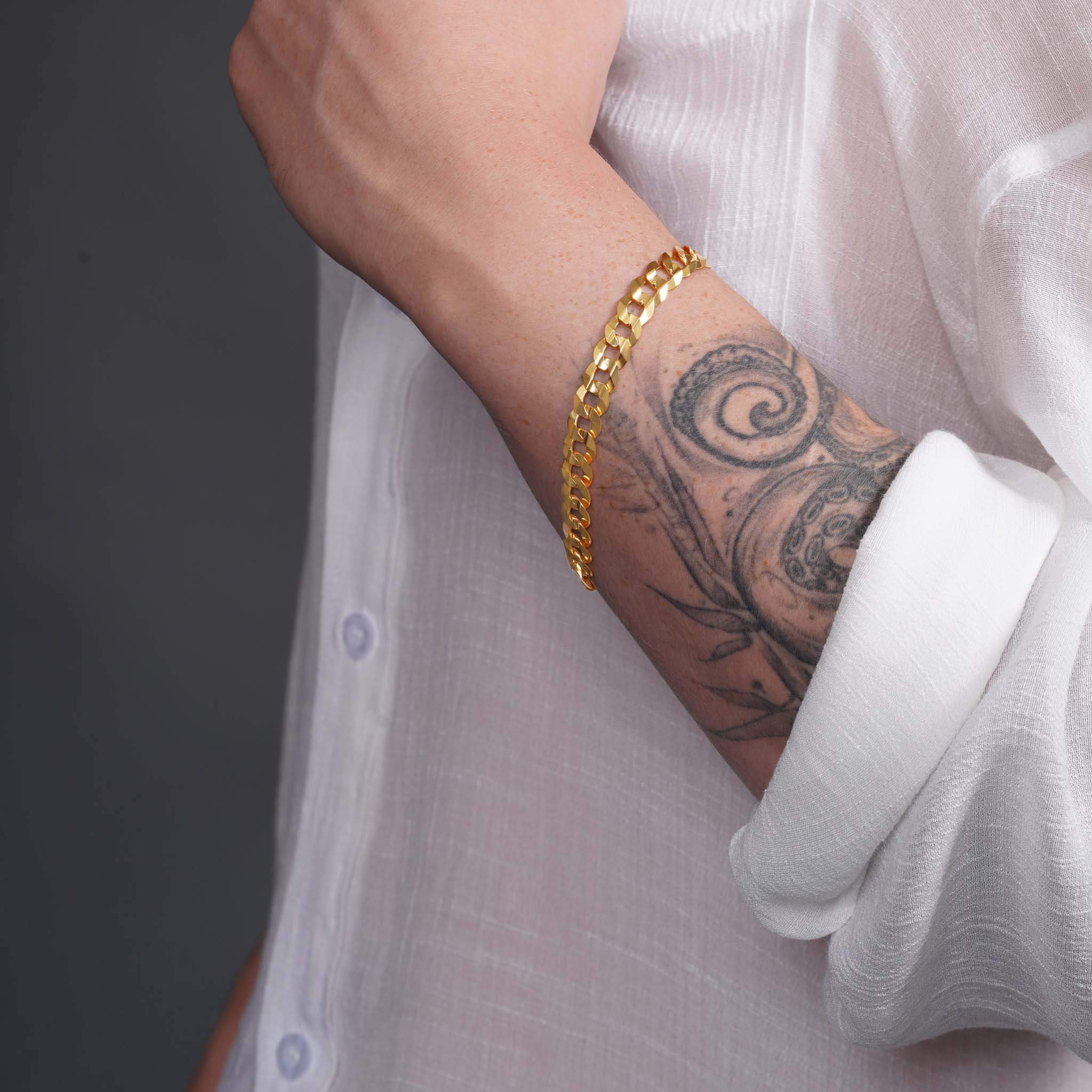 Men's solid gold curb bracelet showcased on a tattooed wrist, highlighting its classic design and luxurious craftsmanship.