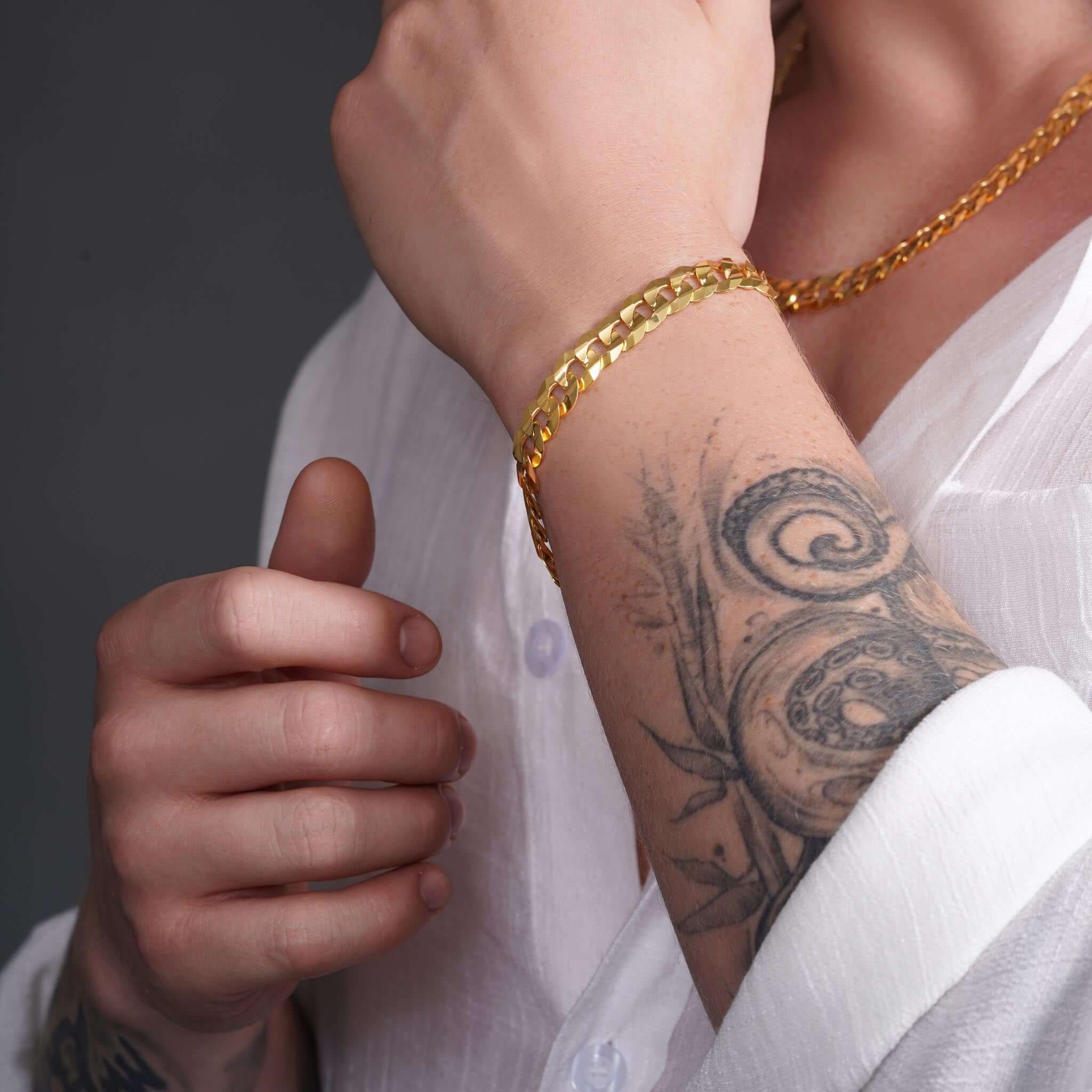 Close-up of a man wearing a 14K gold curb bracelet, showcasing a stylish tattoo and elegant wrist accessory.