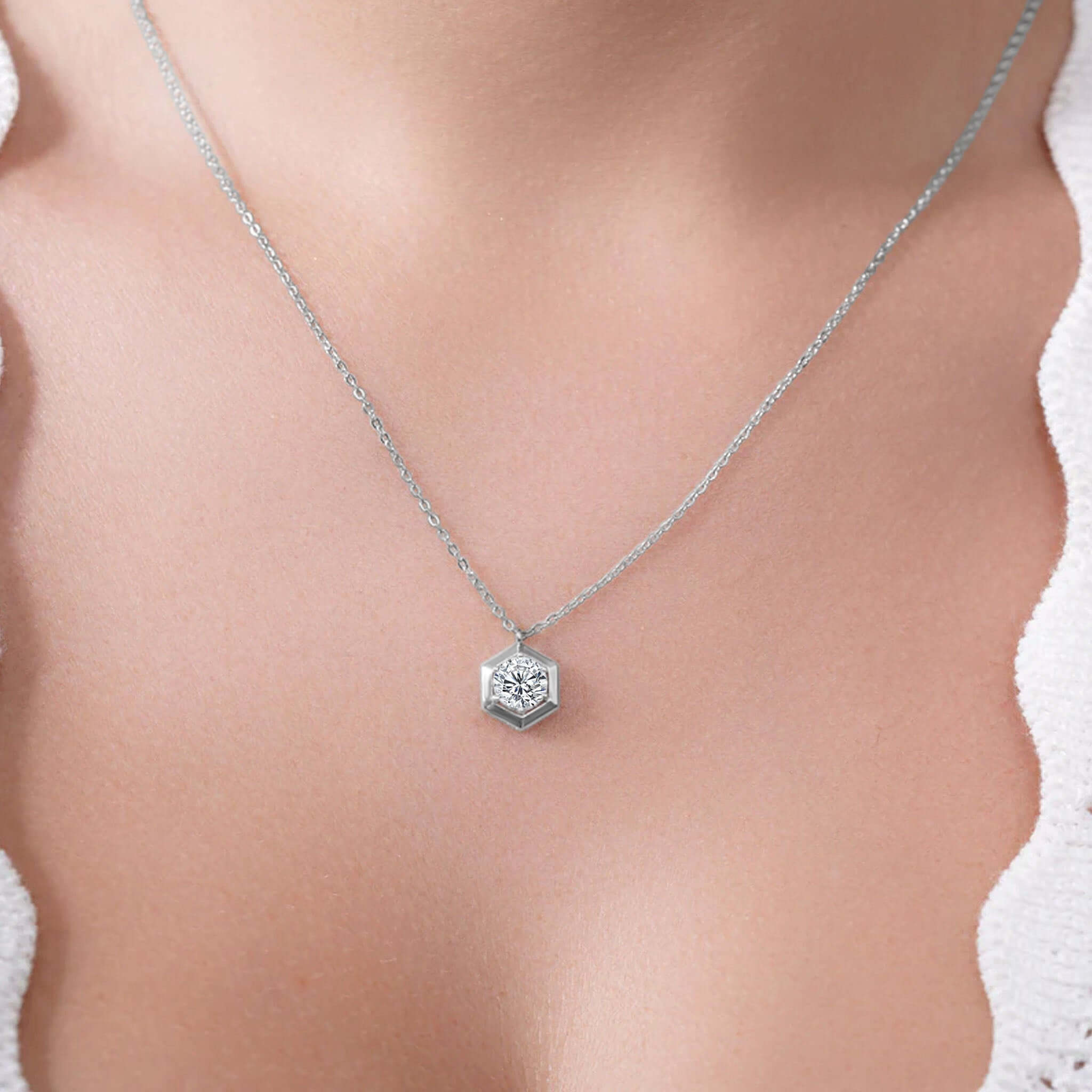 Silver necklace with a hexagonal pendant on a person wearing a white top.